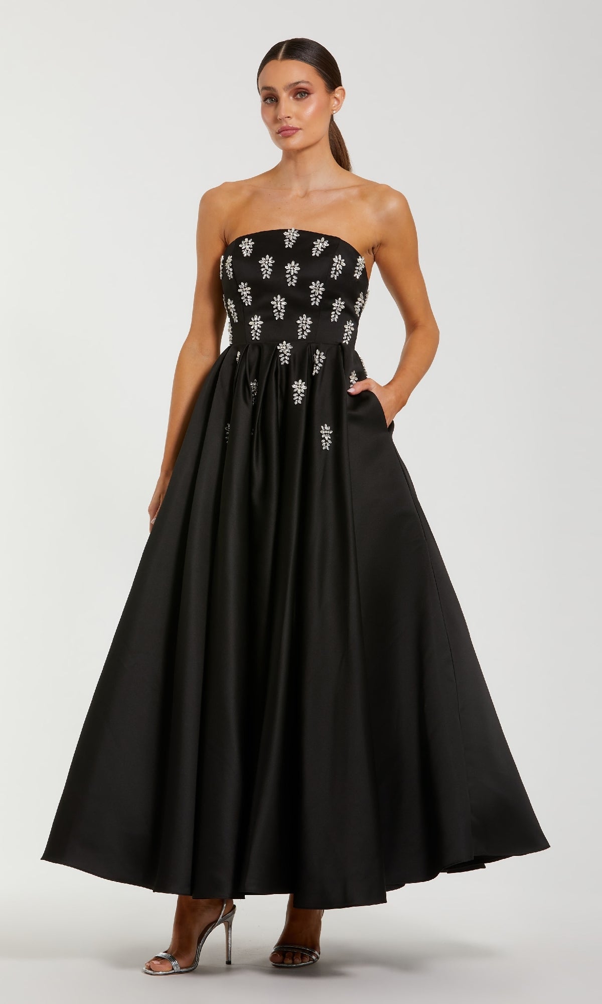 Woman wearing a black strapless dress with pockets on a white background