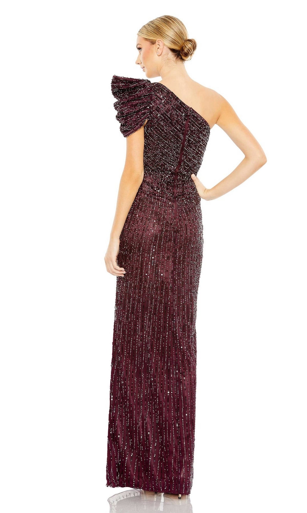 A woman stands facing away, wearing the Long Formal Dress 5622 by Mac Duggal in burgundy, featuring a fitted silhouette, one-shoulder design, beaded detailing, and a textured puff sleeve.