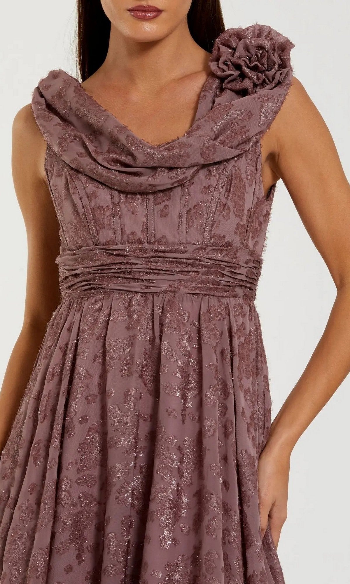 A woman wears the Mac Duggal 56223 midi semi-formal dress, featuring a sleeveless mauve design with a draped cowl neckline, floral patterns, and a large fabric flower accent on one shoulder.