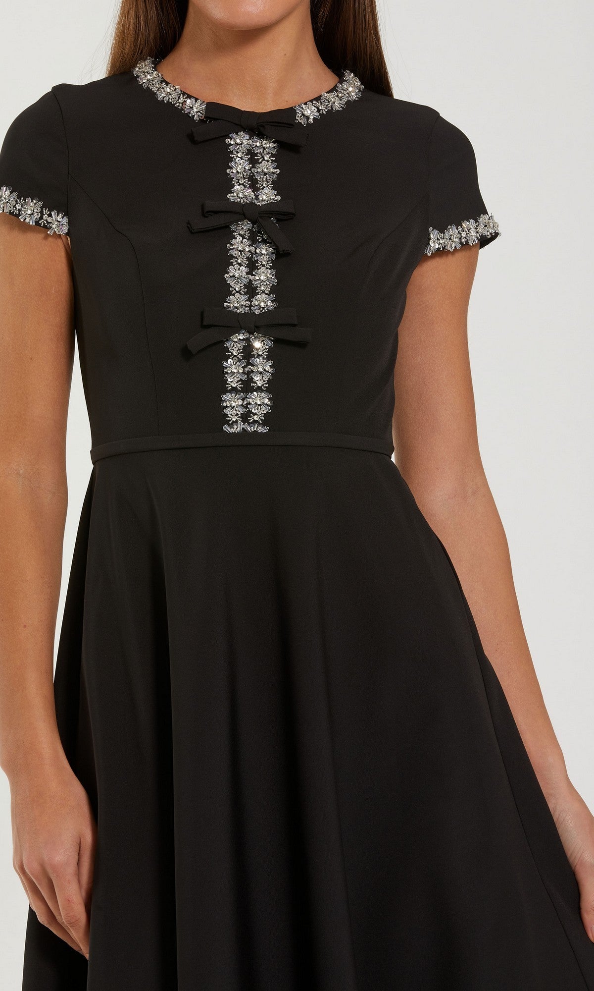 A woman wearing the Mac Duggal 56242 Midi Party Dress—a short-sleeved black dress adorned with decorative silver embellishments and elegant bow details on the front and sleeves—makes a sophisticated choice for a wedding guest outfit.