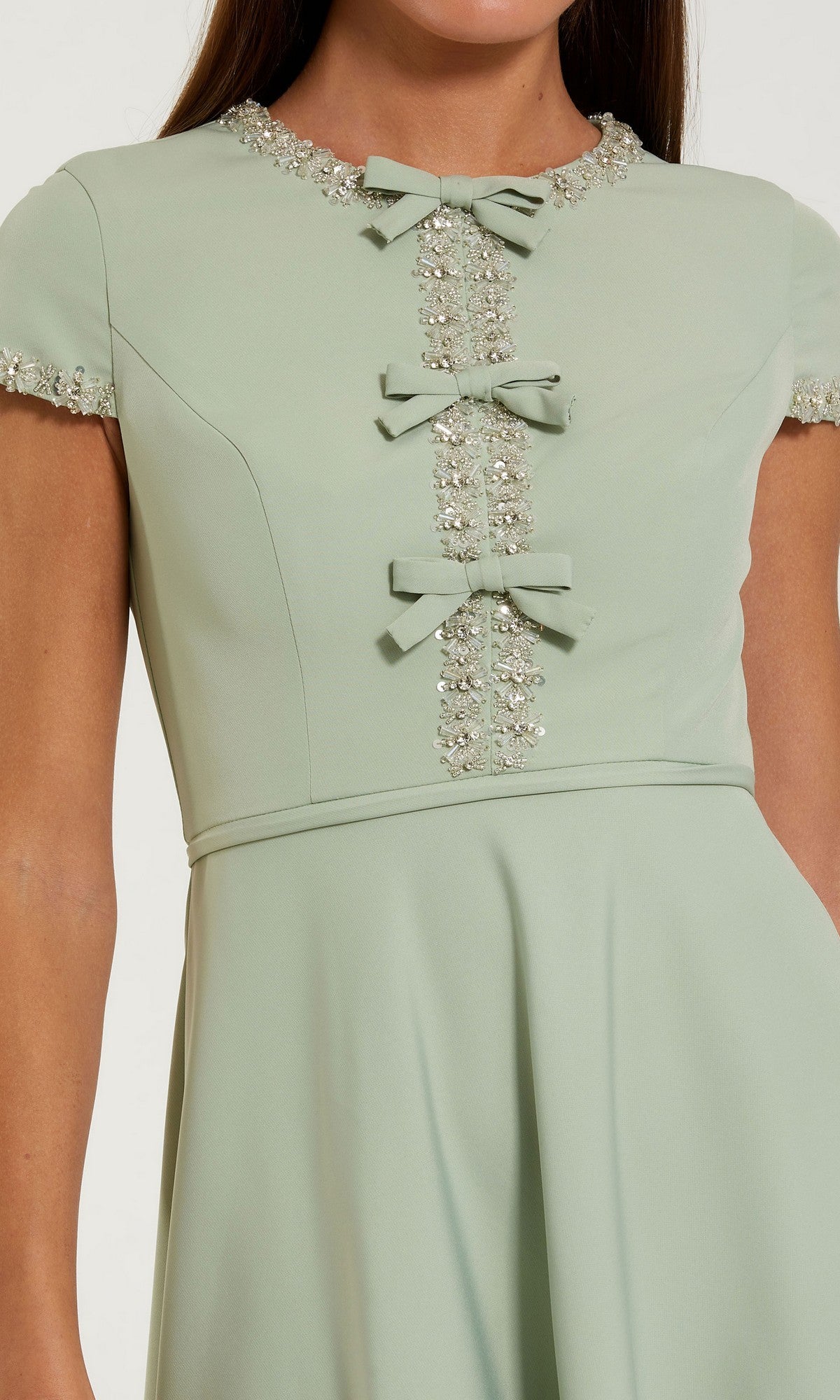 A woman wearing the Mac Duggal 56242 Midi Party Dress in light green, featuring short sleeves, rhinestone embellishments, and delicate small bows down the front—a perfect choice for a wedding guest or as a stylish midi party dress.