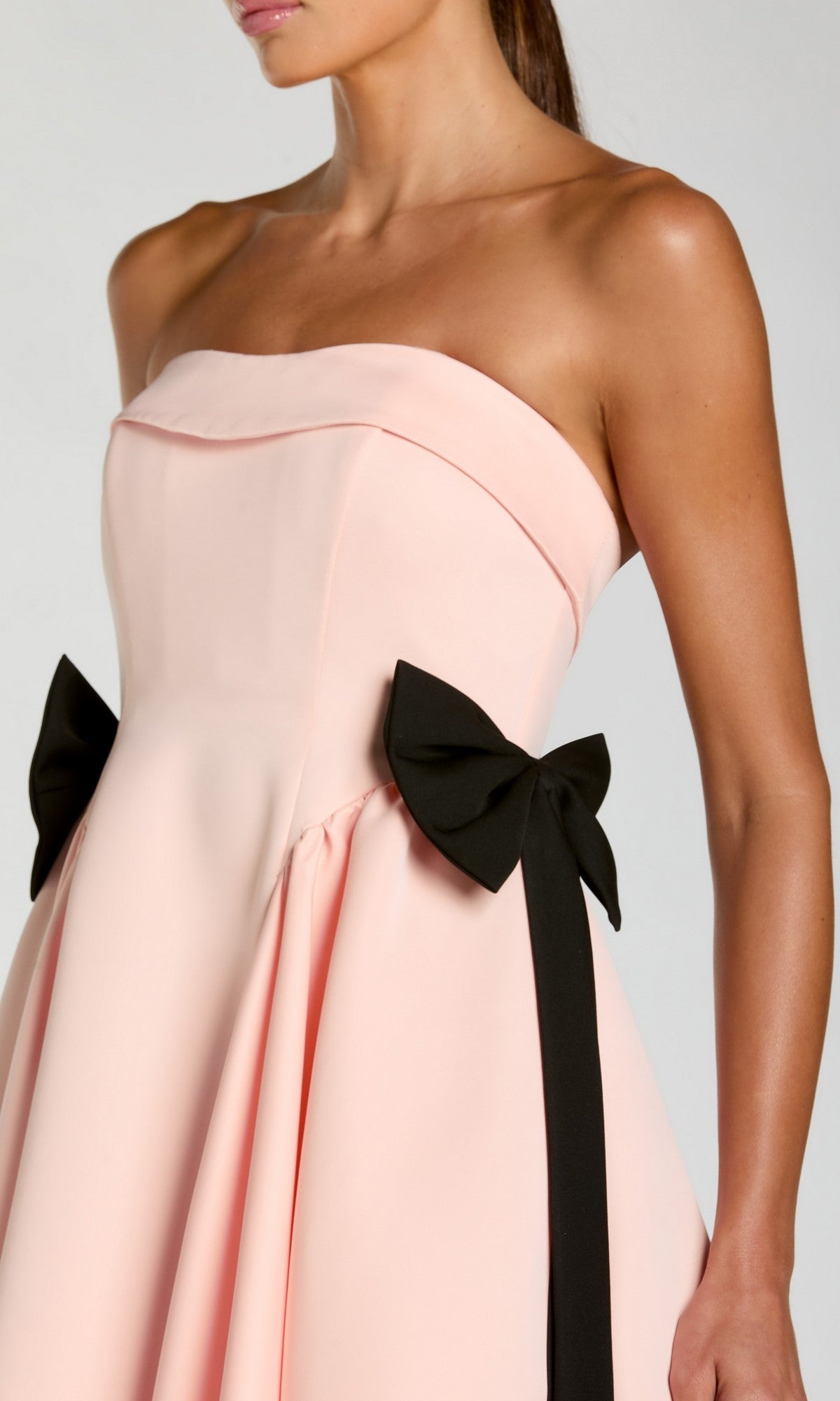 A woman wearing the Mac Duggal 56251 long formal dress in pale pink, featuring a strapless neckline and two black bows at the waist, photographed from the shoulders to mid-thigh.