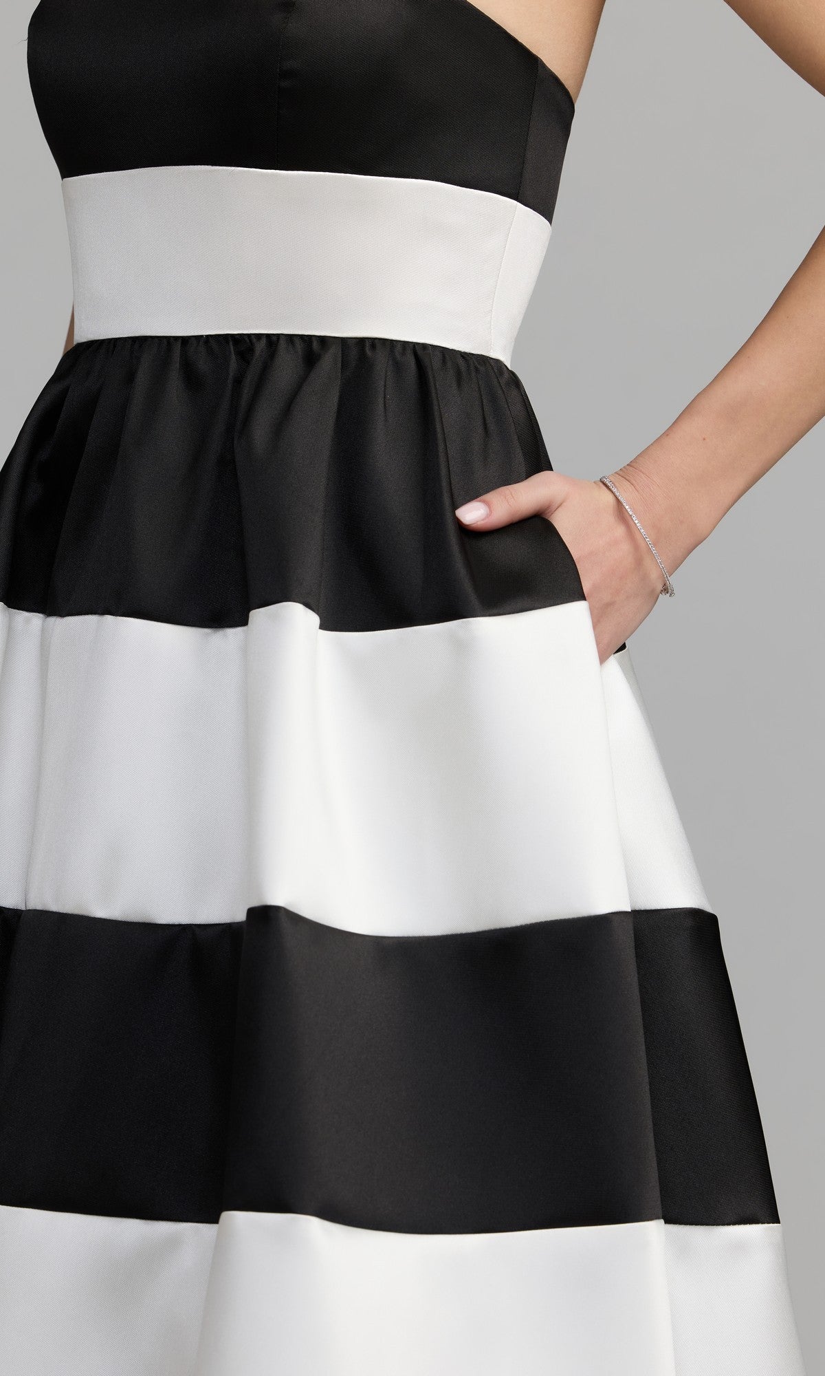 A woman wearing the Mac Duggal 56281 tea-length party dress, featuring wide black and white horizontal stripes; she has one hand in her pocket and a thin bracelet on her wrist.