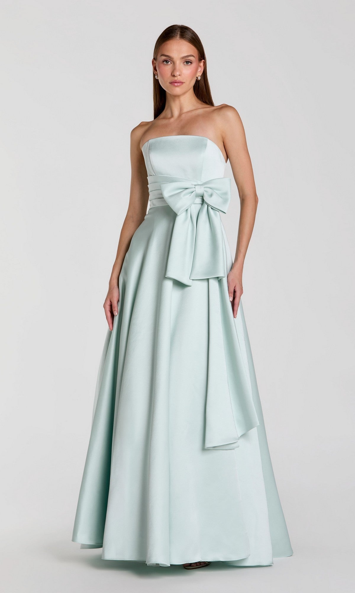 A woman wearing the Long Formal Dress: Mac Duggal 56318 in seafoam, a strapless satin gown with a floor-length silhouette and a large bow at the waist, stands against a plain light background.