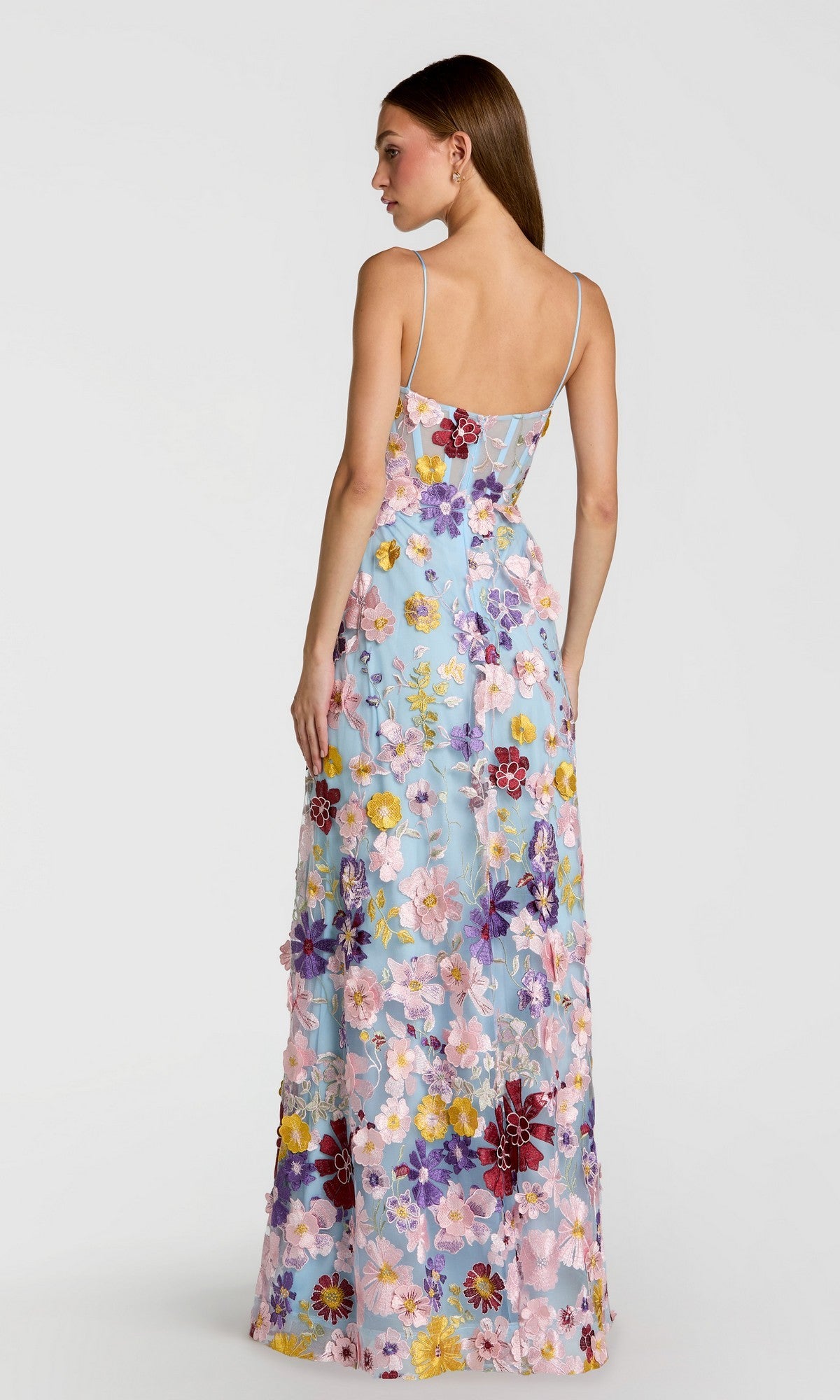 A woman is shown from the back against a plain white background wearing the Long Formal Dress: Mac Duggal 56331, a light blue floor-length gown with colorful floral embroidery.