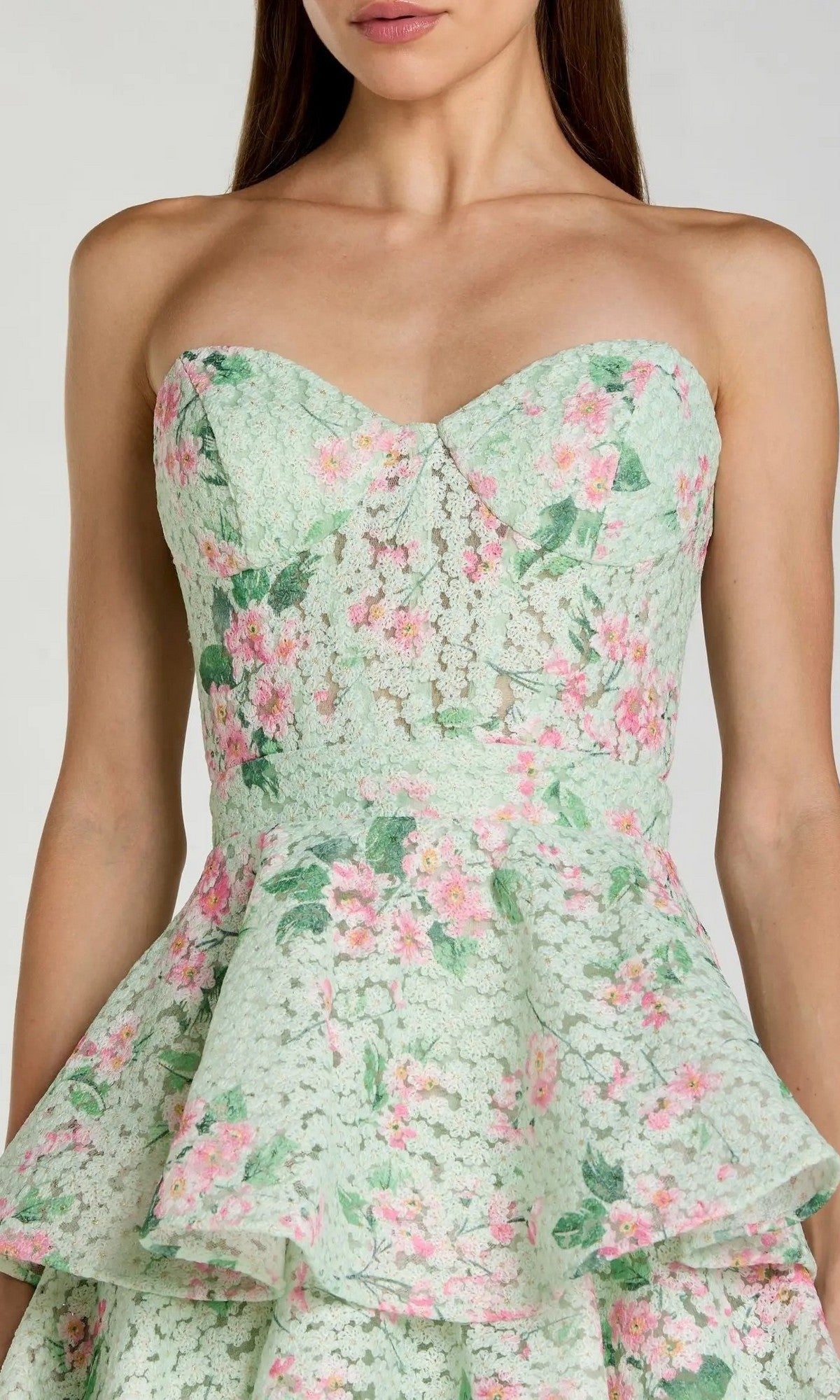 A woman wearing the Midi Wedding Guest Dress: Mac Duggal 56389 — a strapless, mint green midi dress adorned with a pink floral pattern and finished with a peplum ruffle at the waist. This elegant floral-printed net dress provides a fresh and feminine look, making it the perfect choice for wedding guests.