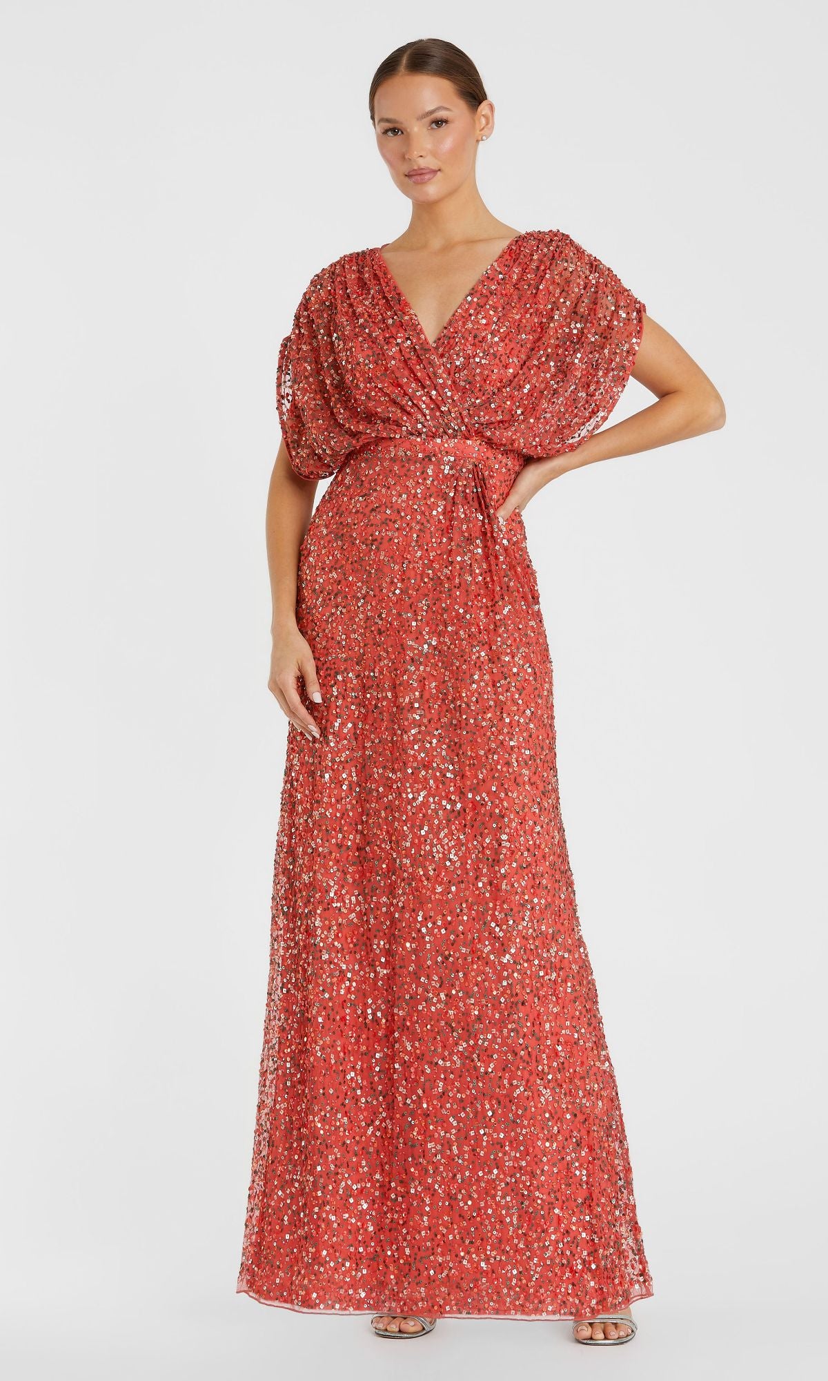A woman poses with one hand on her hip, wearing the Mac Duggal 5640 Short Sleeve Long Sequin Formal Dress in red, featuring a floor-length silhouette and V-neckline, set against a plain white background.
