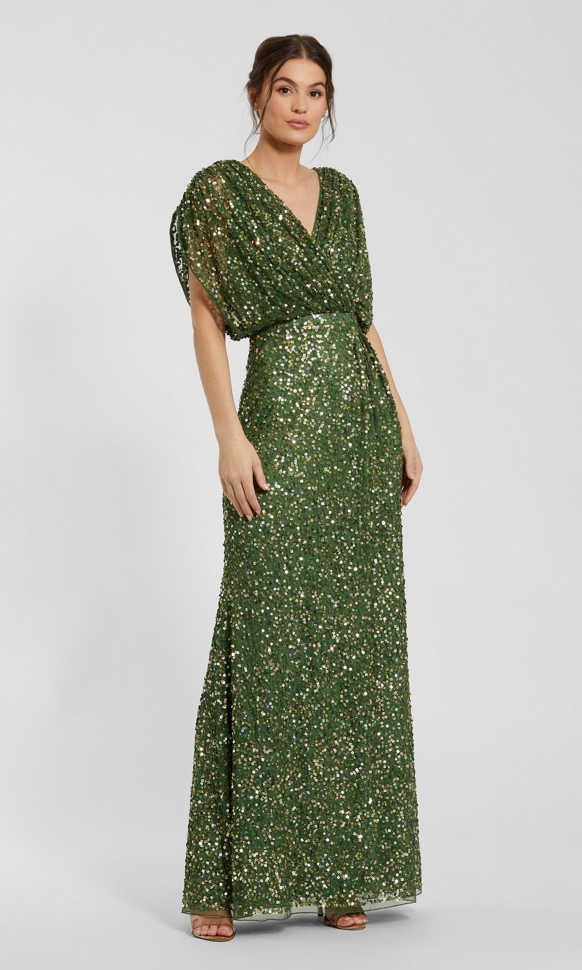 A woman wearing the Mac Duggal 5640 Short Sleeve Long Sequin Formal Dress in sage, featuring a floor-length silhouette, short flutter sleeves, a V-neckline, and a cinched waist, stands against a plain light background.