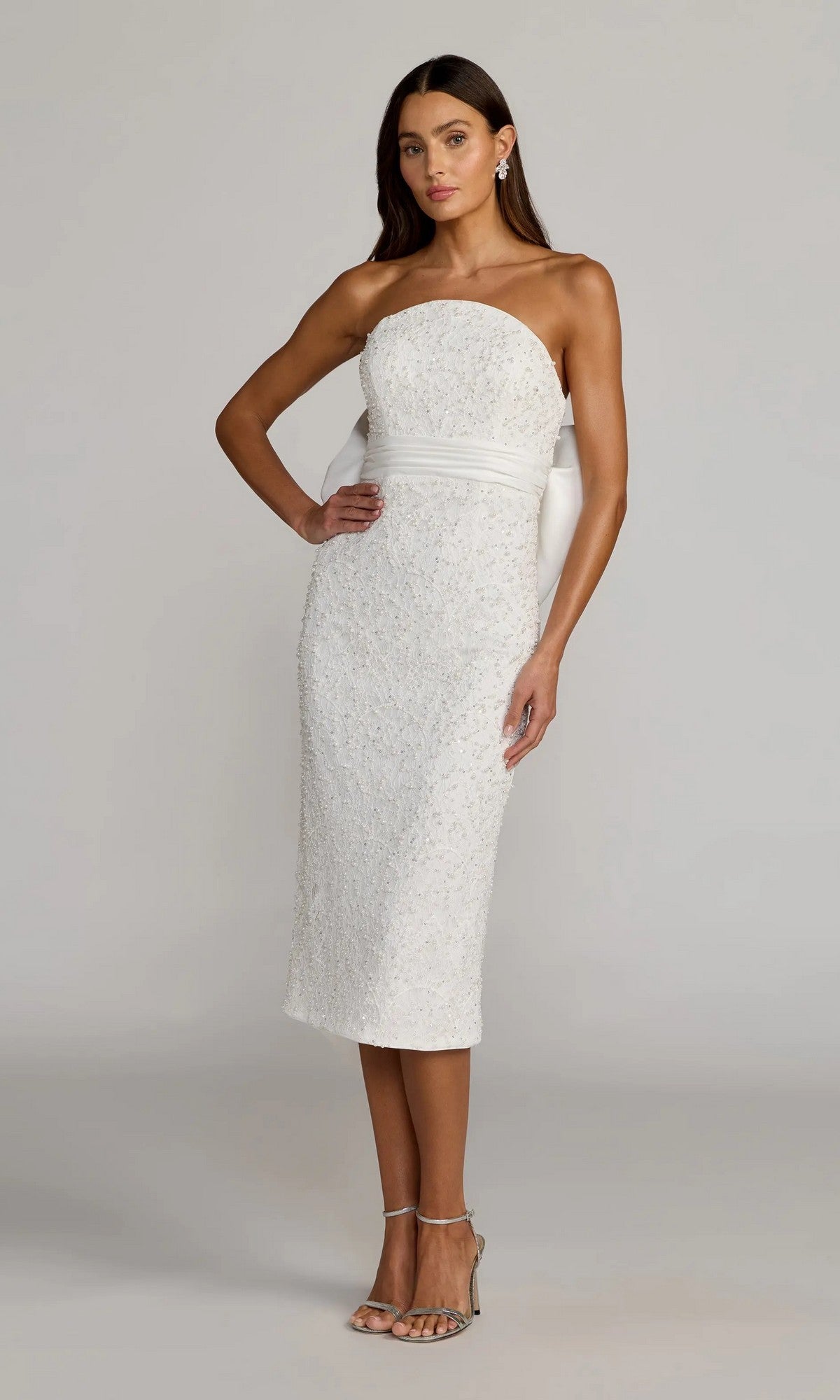 An ivory Mac Duggal 56416 strapless midi party dress with subtle texture is worn by a woman posing with one hand on her hip and strappy heels, set against a neutral background.