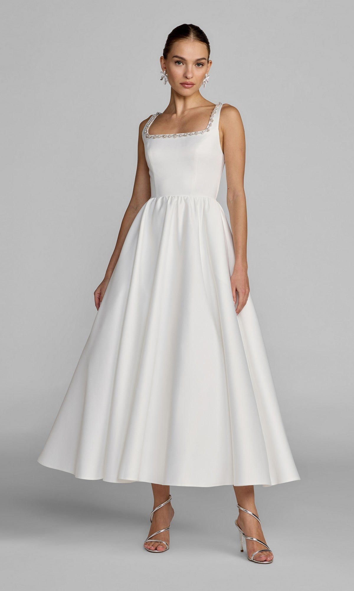 A woman poses against a plain light gray background wearing the Mac Duggal 56417 Tea-Length Party Dress in ivory, featuring a fitted bodice and flared A-line midi skirt. The dress is adorned with pearl beaded embellishments for an elegant touch. She completes the look with silver heels and earrings.