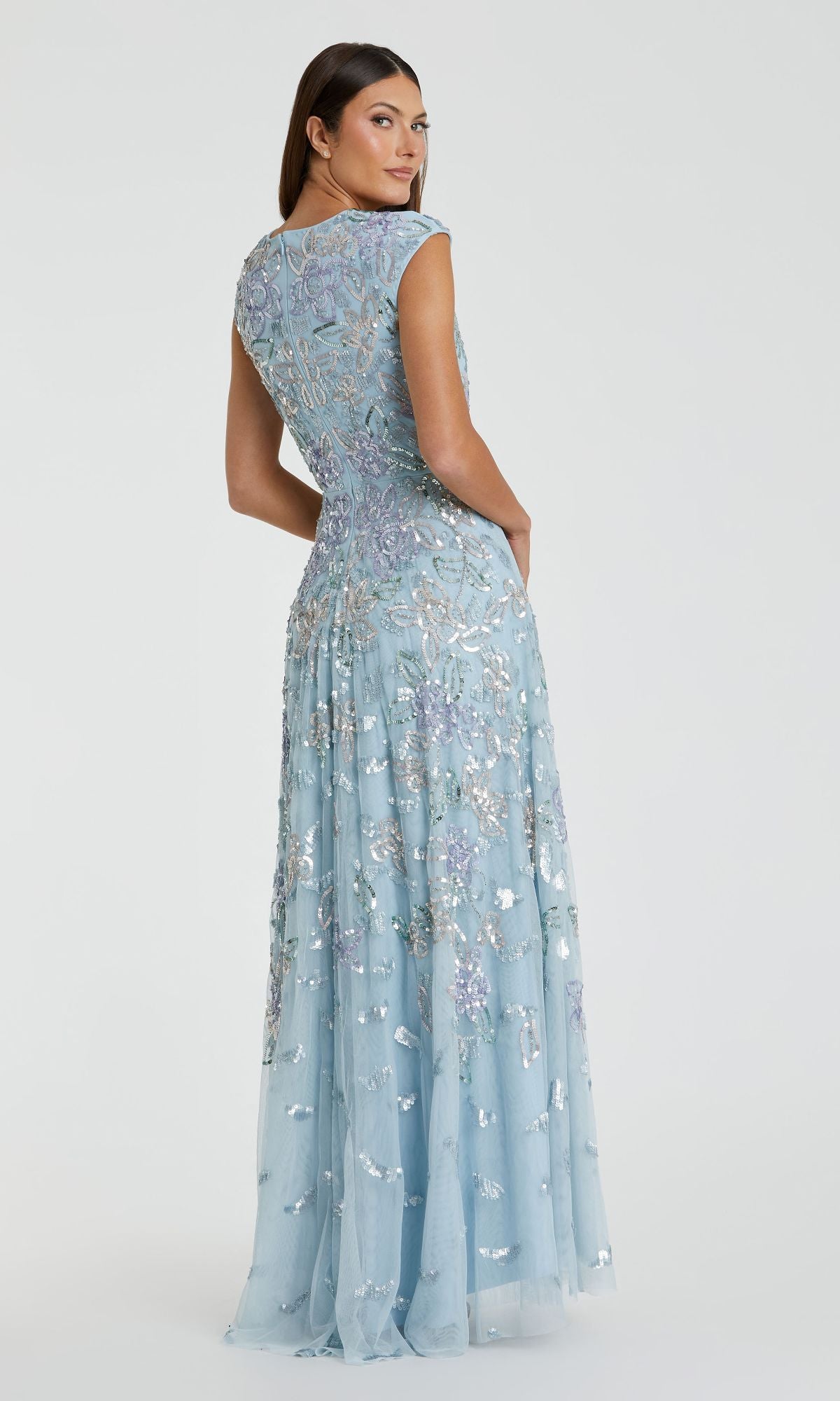A woman, seen from behind, wears the Mac Duggal 5647 Long Blue Sequin Formal Dress with cap sleeves and silver sequin embellishments, set against a simple light background.