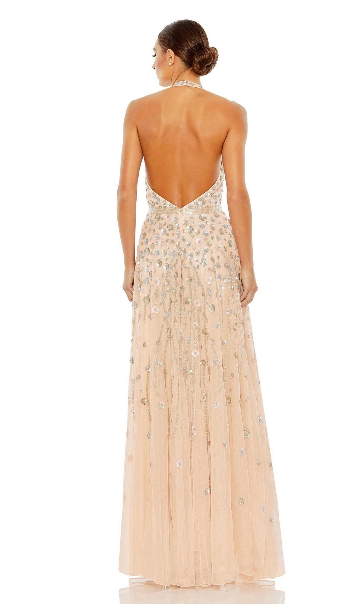 A woman with a low bun wears the Long Formal Dress 5654 by Mac Duggal, a blush halter-neck gown with floral beading, sequin embellishments, floor-length silhouette, and backless design.