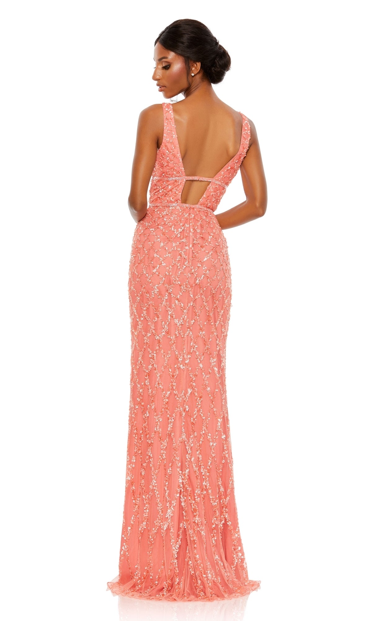 A woman stands facing away from the camera, showcasing a floor-length, sleeveless coral Mac Duggal 5669 Backless Long Beaded Formal Dress with sequin embellishments and an open back.