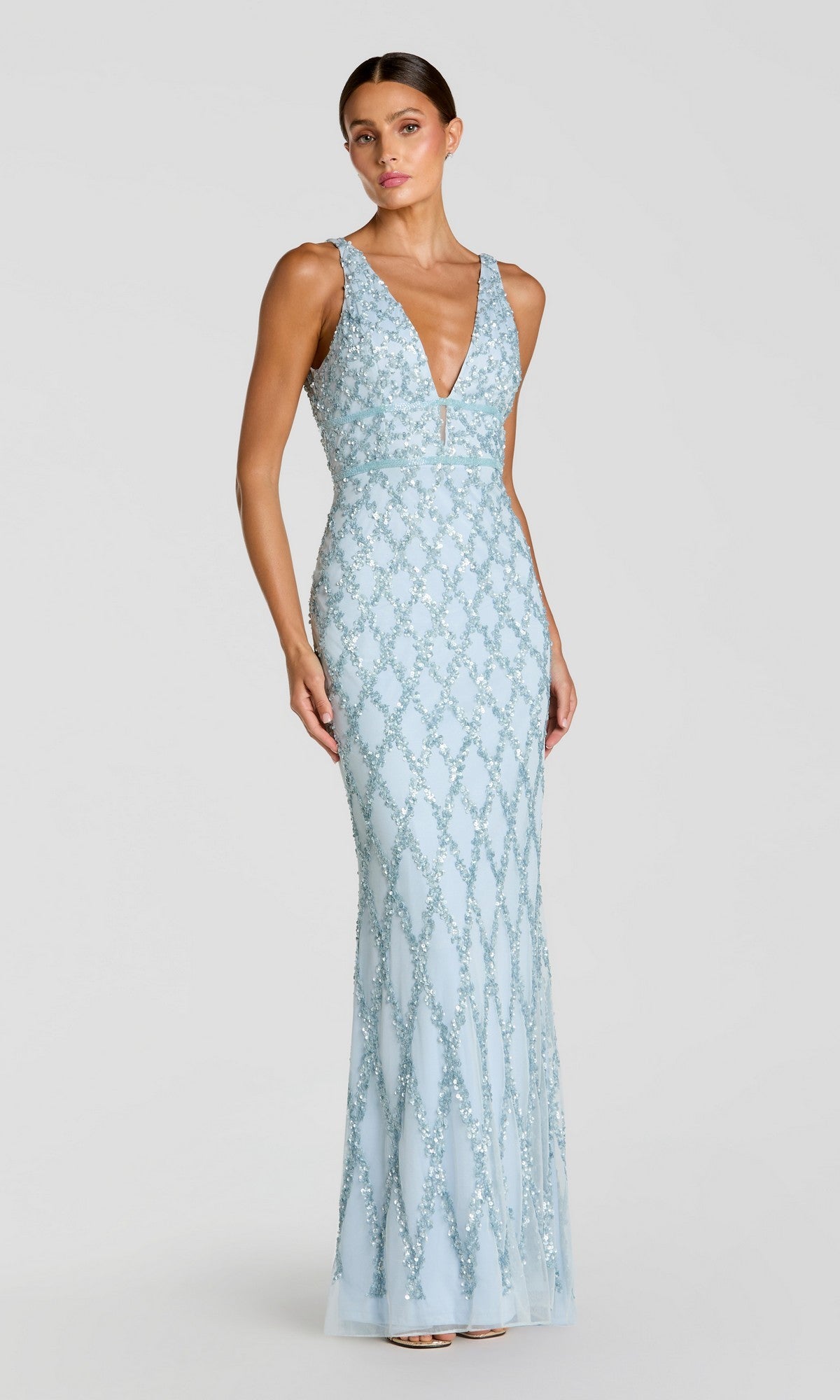 A woman models the Mac Duggal 5669 Backless Long Beaded Formal Dress, a light blue, floor-length sleeveless gown with a deep V-neck and intricate beading, against a plain light backdrop.