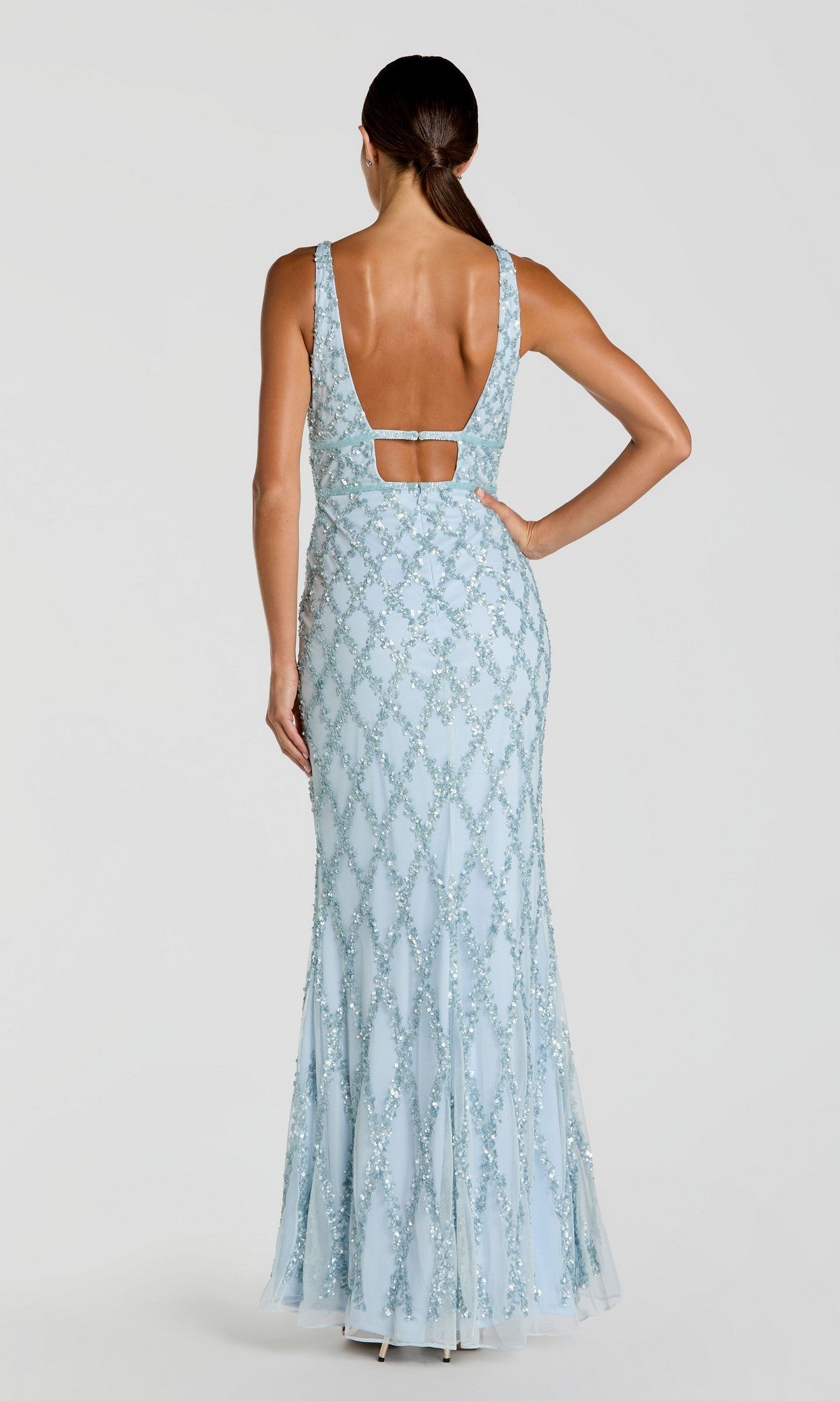 Model wearing the Mac Duggal 5669 Backless Long Beaded Formal Dress—a light blue, floor-length sequin gown with an open back and horizontal strap—stands with one hand on her hip, facing away.