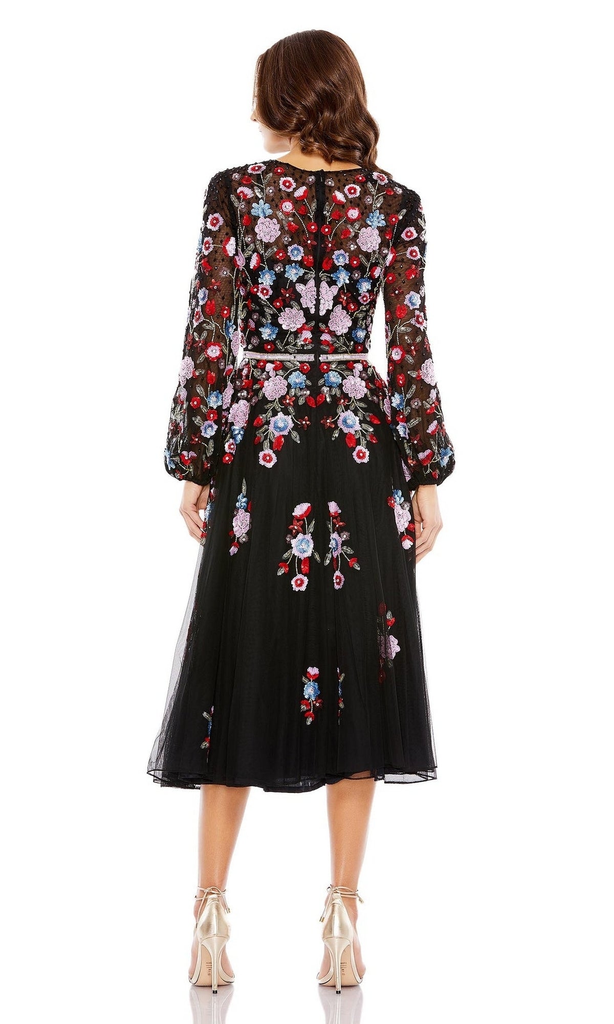 A woman faces away wearing the Mac Duggal Short Semi-Formal Dress 5712, a black long sleeve dress with colorful floral embroidery and beading, styled with beige high heels.