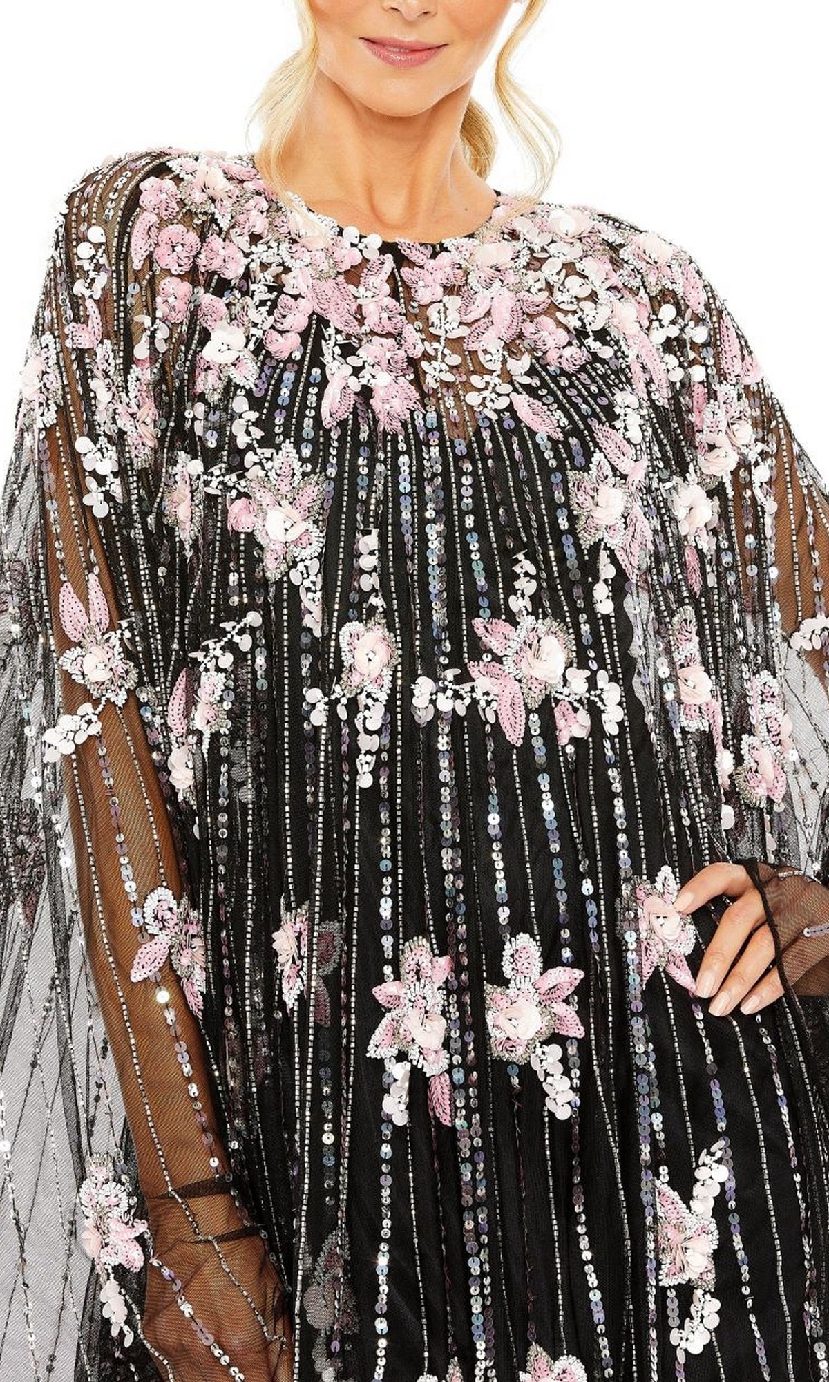 A woman wearing the Mac Duggal 5917 Beaded-Cape Short Hoco Dress, a sheer black cocktail dress embellished with pink and white floral embroidery, sequins, and beading.