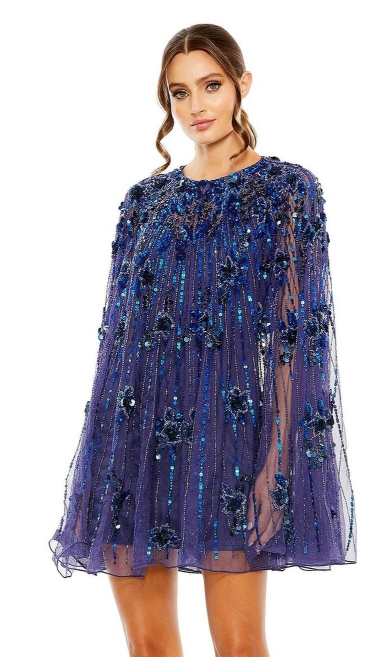 Woman wearing the Mac Duggal 5917 Beaded-Cape Short Hoco Dress, a royal blue homecoming dress featuring sequins and floral embellishments, standing against a plain white background.