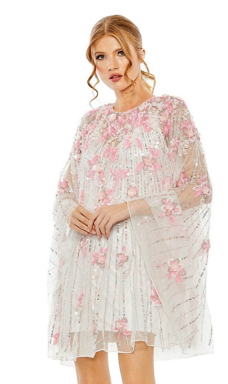 A woman models the Mac Duggal 5917 Beaded-Cape Short Hoco Dress, featuring a sheer embellished cape over a chic short dress, set against a plain white background.