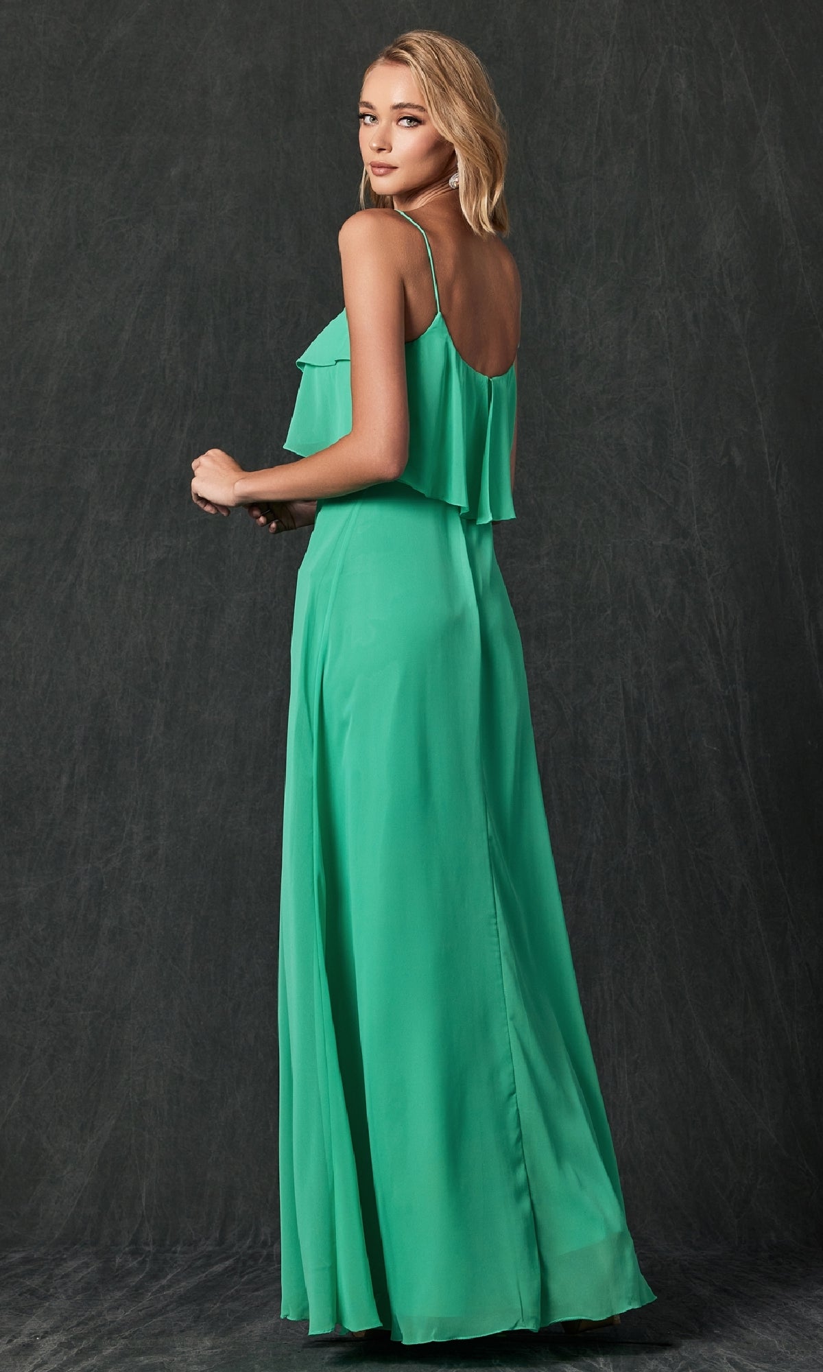 A woman poses in the Juliet 591, a sleeveless, floor-length green wedding-guest dress with a pop-over bodice, set against a dark, textured background.