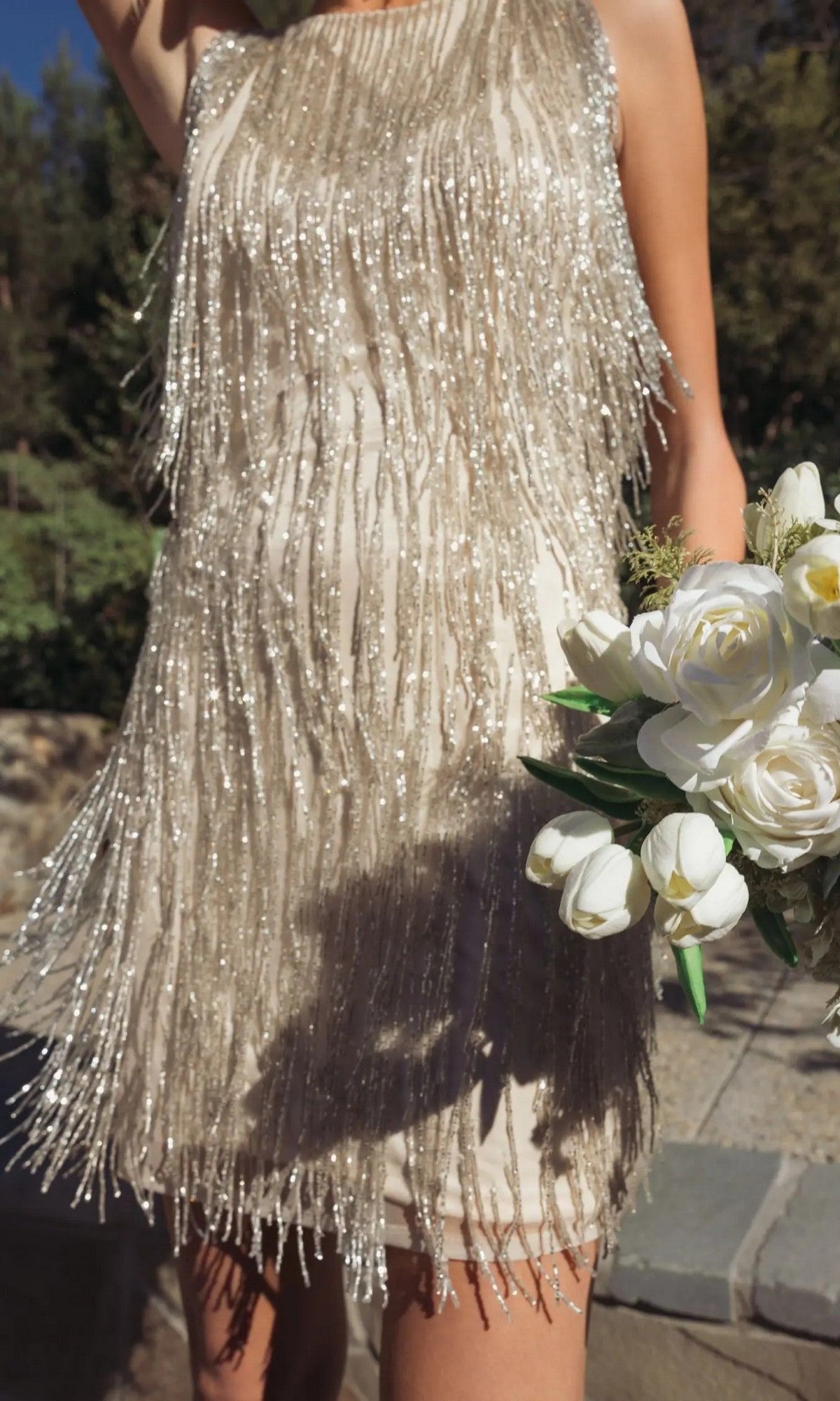 Person in a Mac Duggal 5934 Short Beaded Fringe Party Dress, sleeveless and black, holding a bouquet of white flowers outdoors.