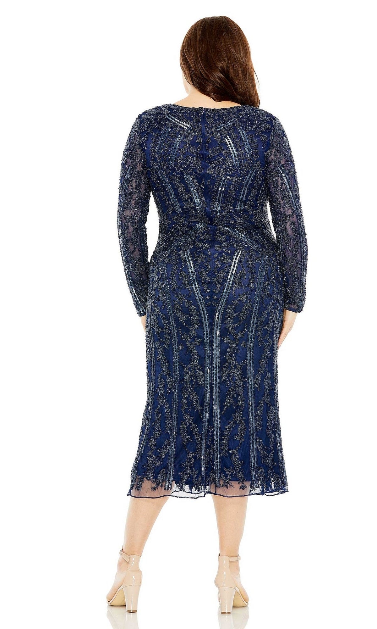 A woman stands facing away in the Plus Size Wedding Guest Dress 5938 by Mac Duggal—a navy blue, beaded midi dress with long sleeves and intricate lace detail, paired with nude heels.