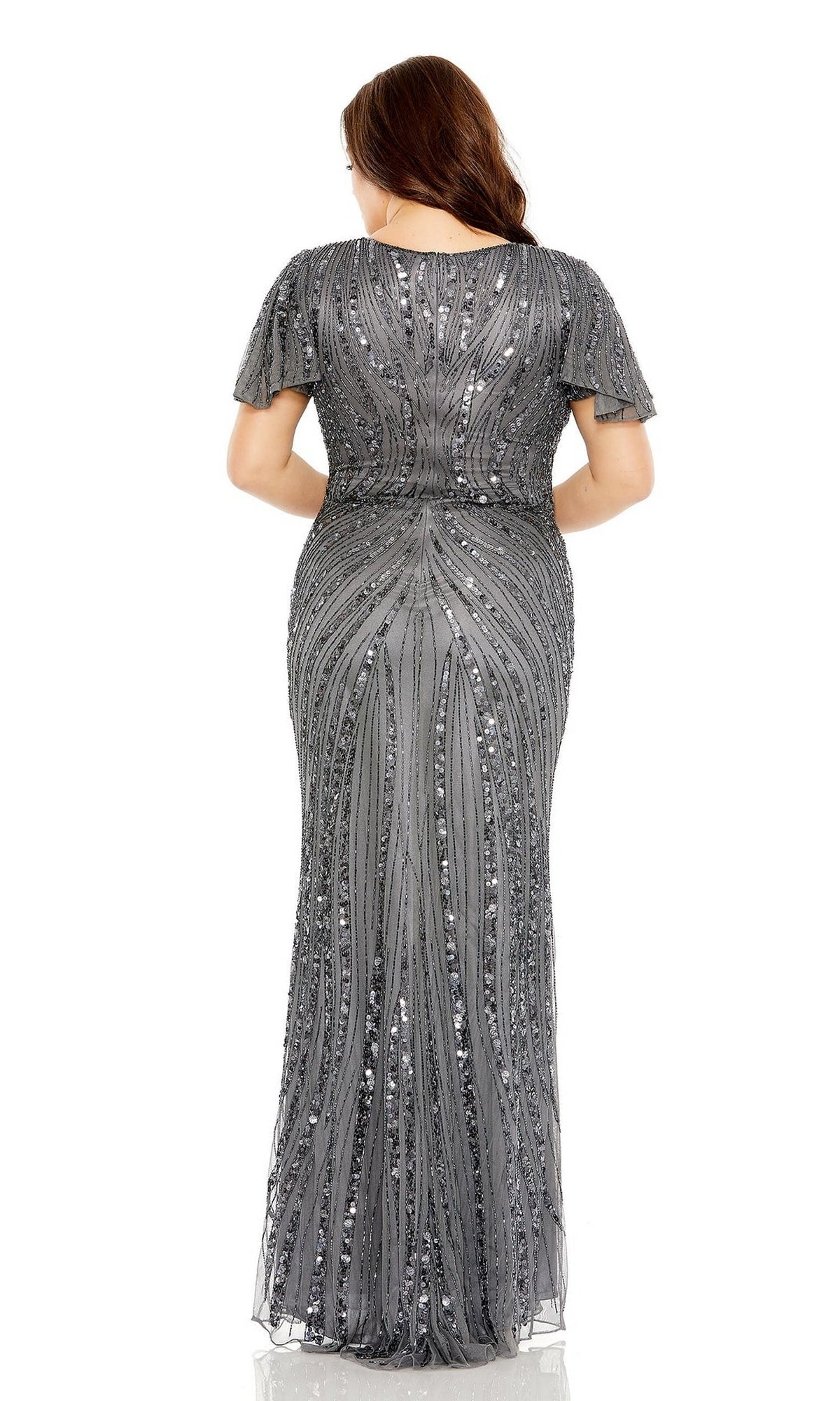 A woman faces away, wearing the Long Plus-Size Prom Dress 5945 by Mac Duggal—a floor-length, short-sleeved silver gown adorned with intricate sequin and beaded patterns on a white background.