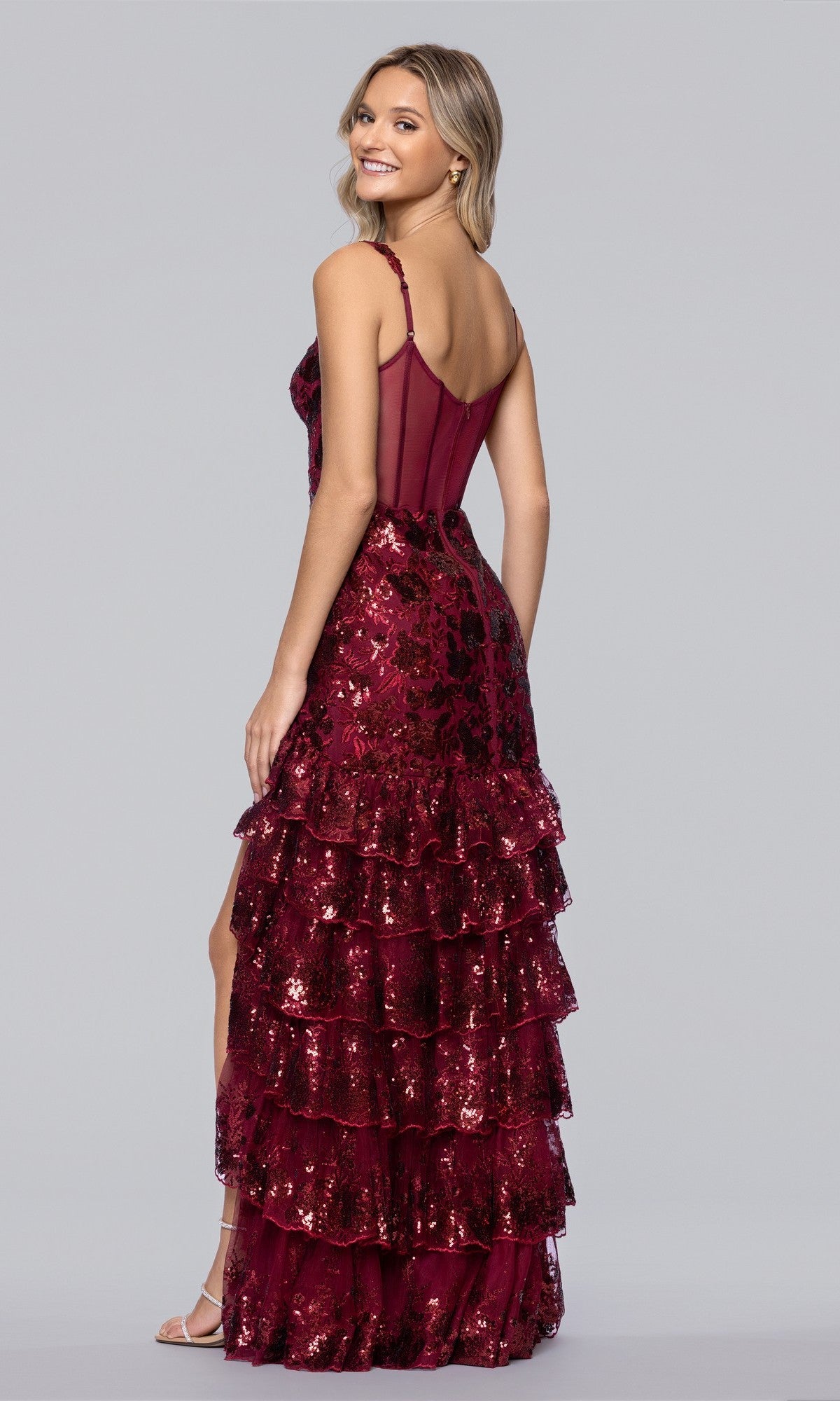 A woman models the Blondie Nites 5962BN long prom dress, featuring a sleeveless sequin bodice and tiered ruffle floor-length skirt, standing sideways and looking over her shoulder against a plain background.