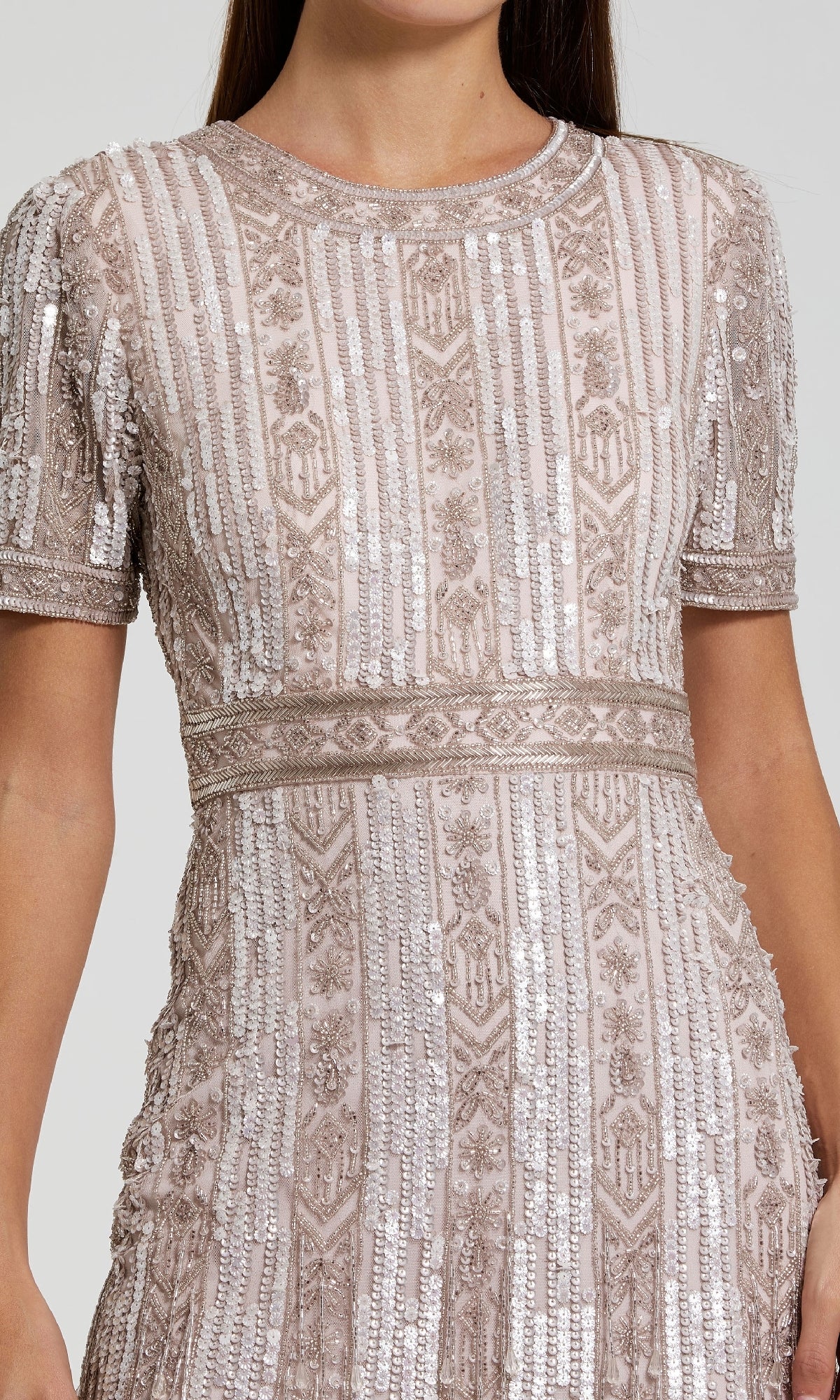 A woman wearing the Midi Fringe Wedding-Guest Dress: Mac Duggal 5980, a light pink short sleeve midi dress with intricate beadwork, sequins, and geometric patterns; shown from shoulders to mid-thigh.