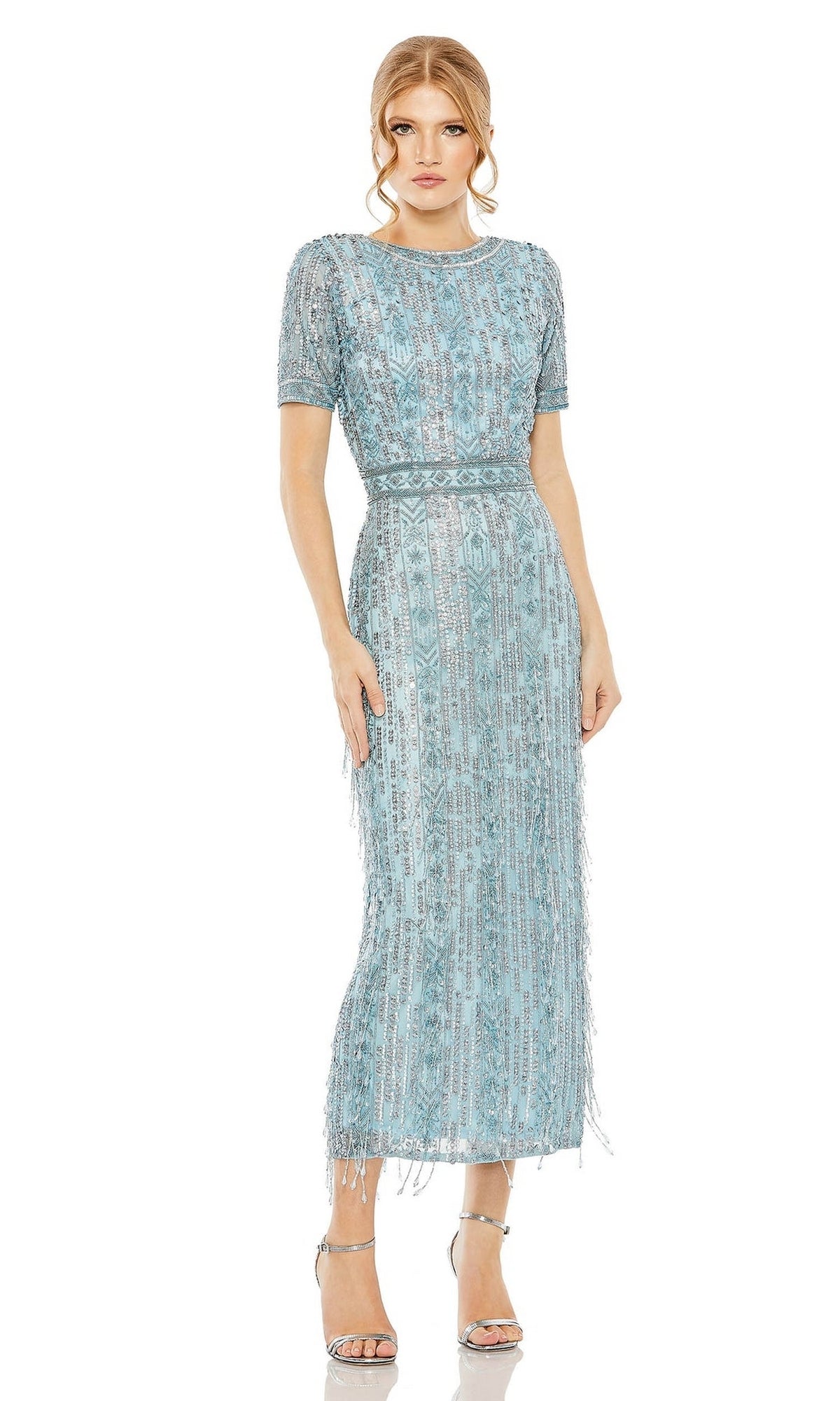 A woman stands against a white background wearing the Mac Duggal 5980 Midi Fringe Wedding-Guest Dress, featuring light blue fabric, short sleeves, beaded fringe details, and silver high-heeled sandals.