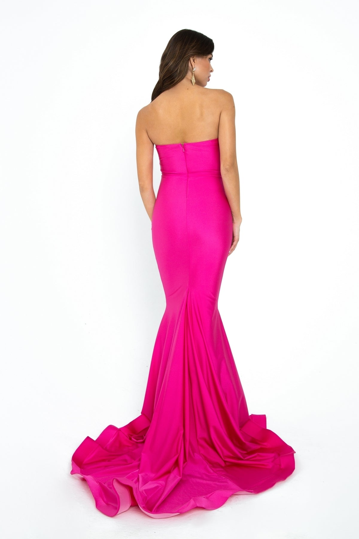 A woman in the Strapless Sleek Long Prom Dress: Atria 6028H poses with her back to the camera, its vibrant pink mermaid skirt flowing gracefully on the floor against a white background.