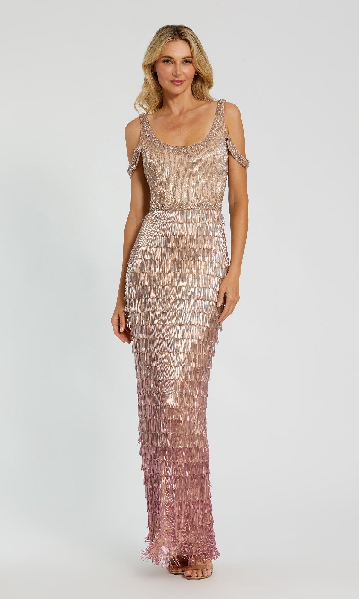 A woman stands against a plain light background wearing the Fringed Pink Ombre Formal Dress: Mac Duggal 6032, a sleeveless, floor-length gown with shimmering pink and gold layers and beaded fringe details.