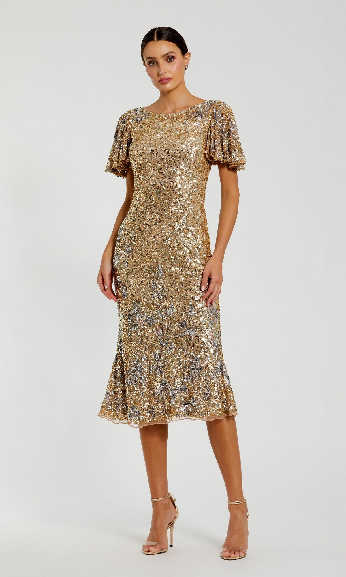 Woman stands wearing the Mac Duggal 6118 Sequin Wedding-Guest Midi Dress in Nude Gold, featuring short sleeves and shimmering gold sequins, paired with nude high-heeled sandals against a plain light background.