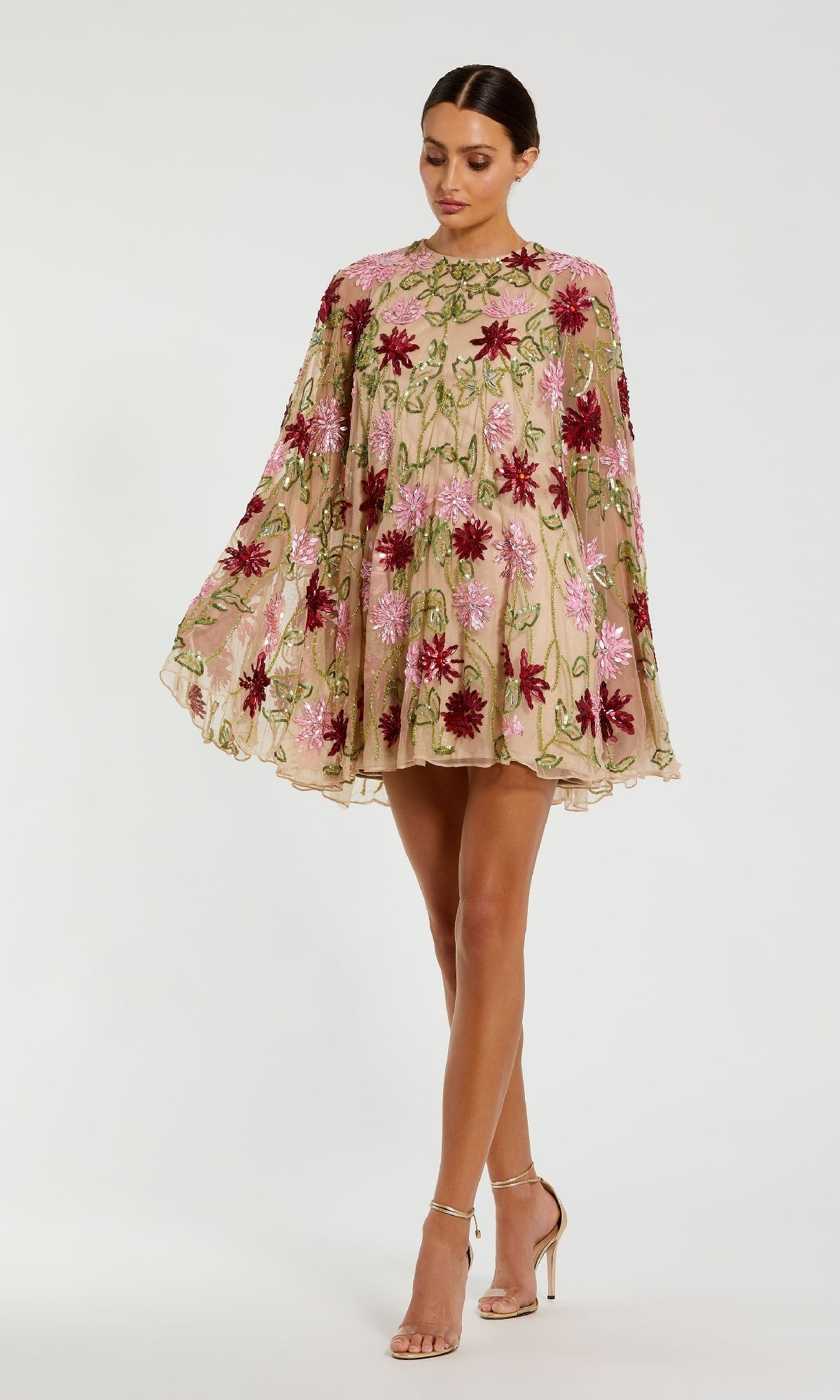 A woman wears the Mac Duggal 6123 Sequin Short Wedding Guest Dress, a beige loose-fit style with pink and red floral embroidery, paired with nude heels against a plain background—ideal as a sequin floral party dress.