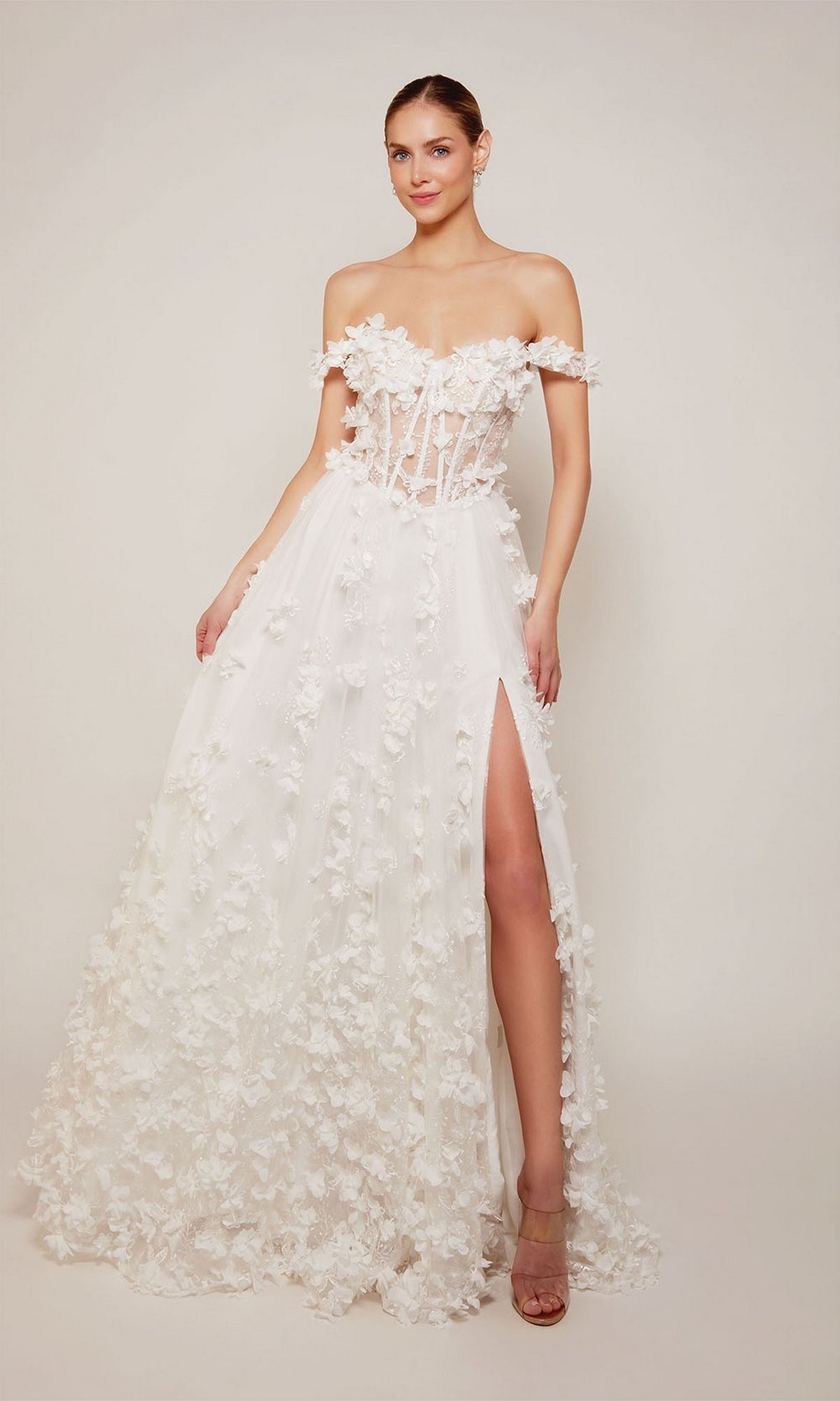 A woman stands against a plain background wearing the Alyce 61308 Off-Shoulder Long Floral Dress, featuring floral appliqués, a sheer corset bodice, and a high slit.