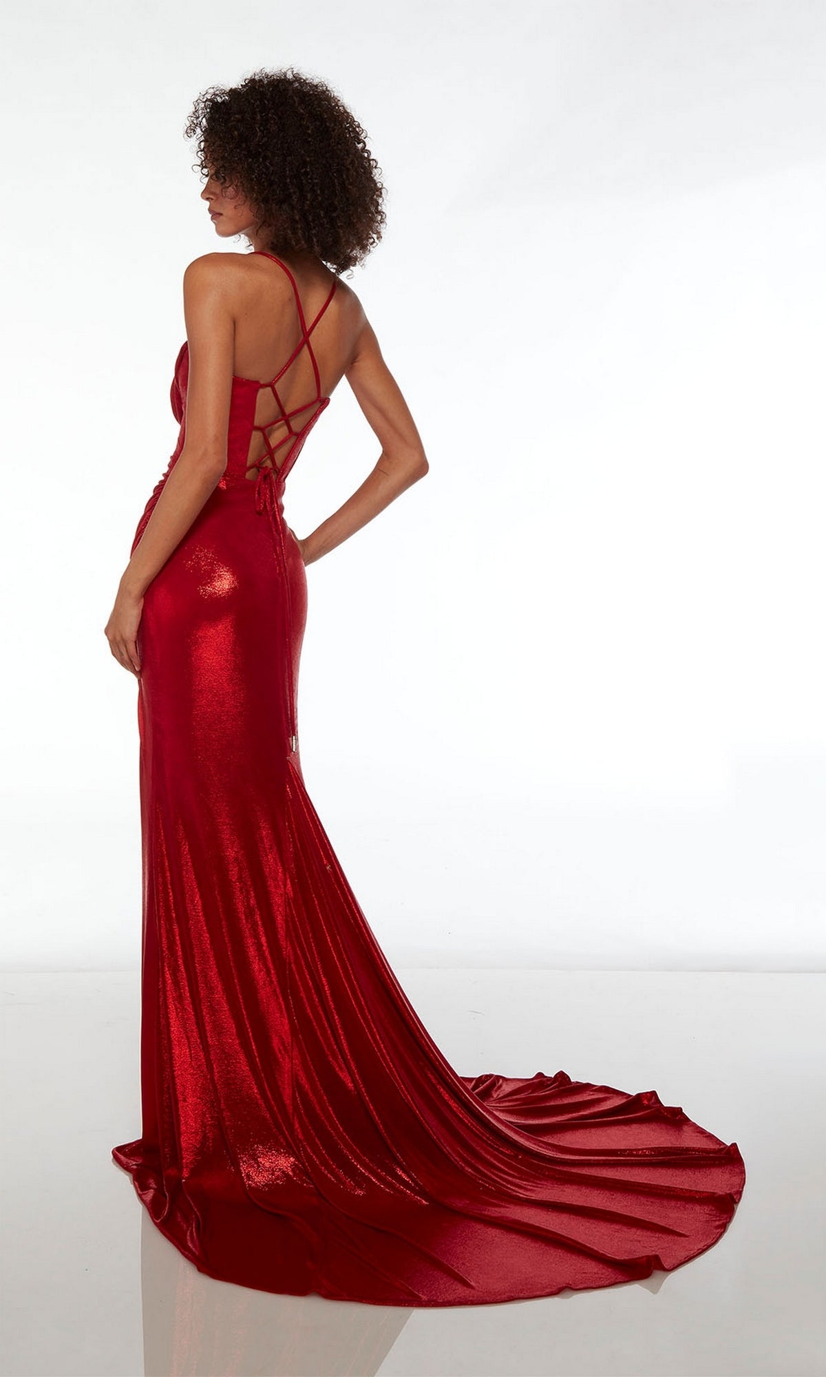 A woman poses with her back to the camera in an Alyce Strappy-Back Long Metallic Prom Dress 61490, featuring a metallic red finish, crisscross straps, and a long train, set against a plain white background.