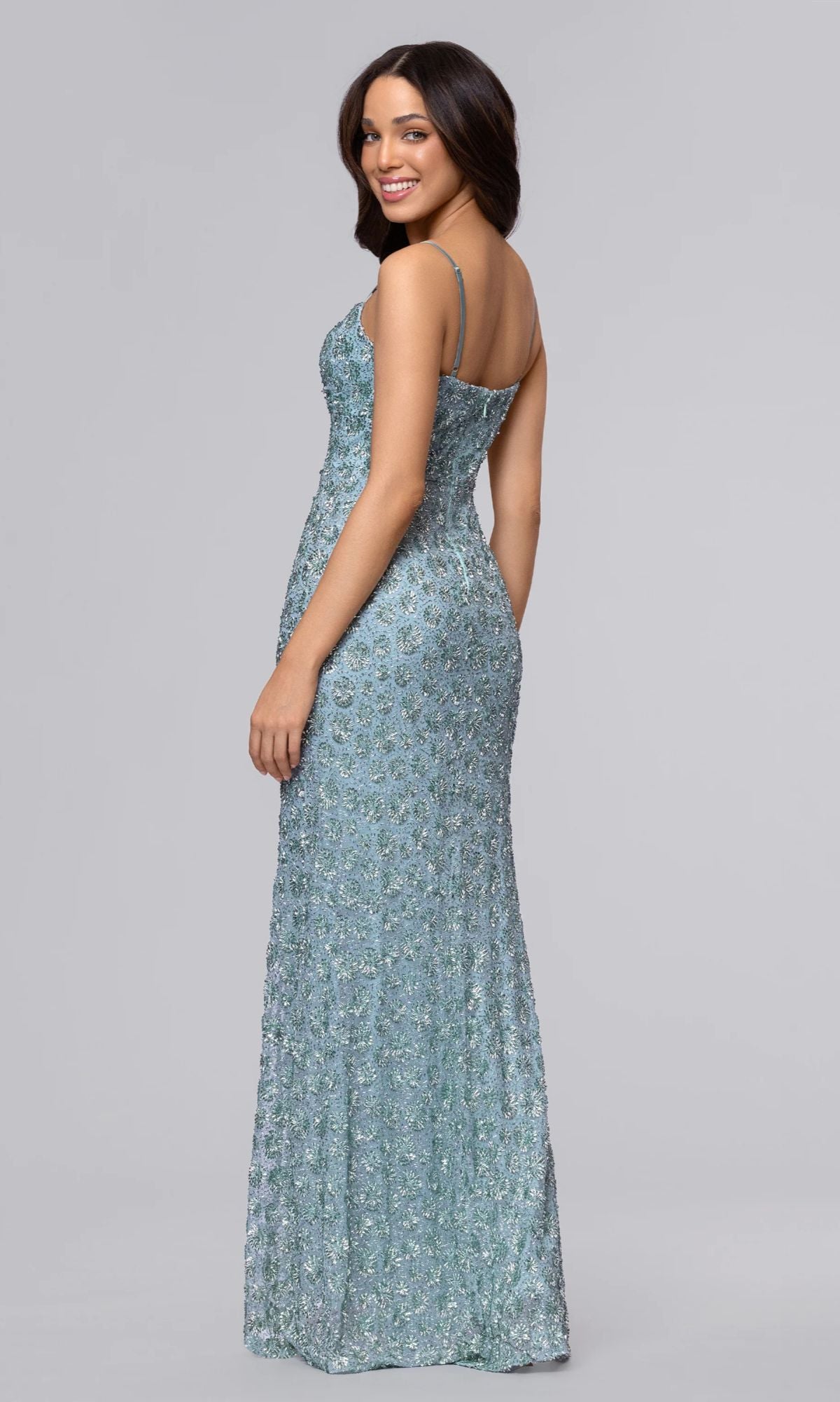 A woman models the Blondie Nites 6171BN, a light blue, floor-length prom dress with adjustable spaghetti straps and shimmering beadwork, posing against a plain gray background.