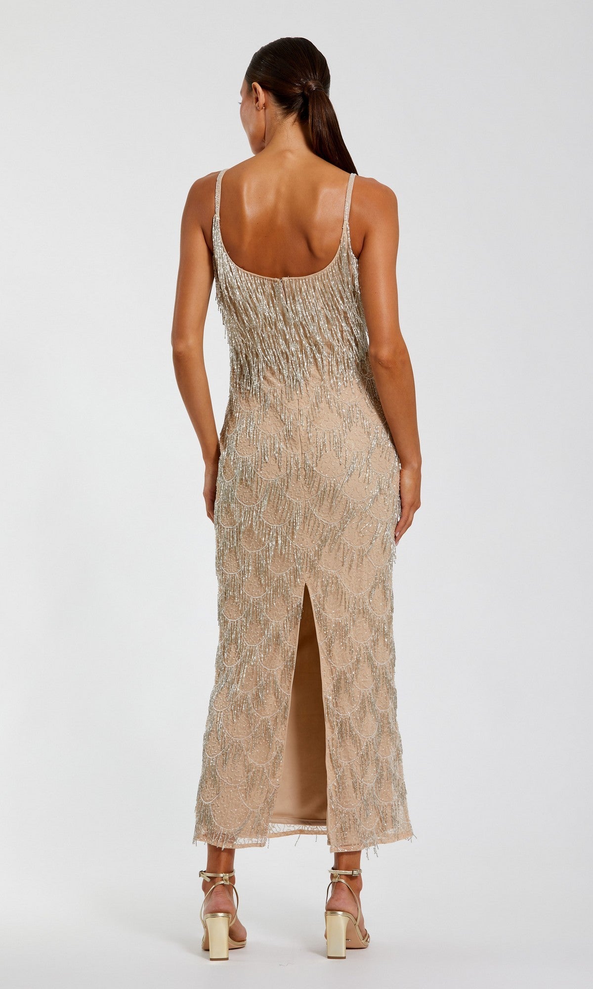 A woman stands with her back to the camera, wearing the Mac Duggal 6172 Long Formal Dress—a sleeveless midi dress featuring intricate beaded fringe details and a back slit—paired with strappy heels, all set against a plain white background.