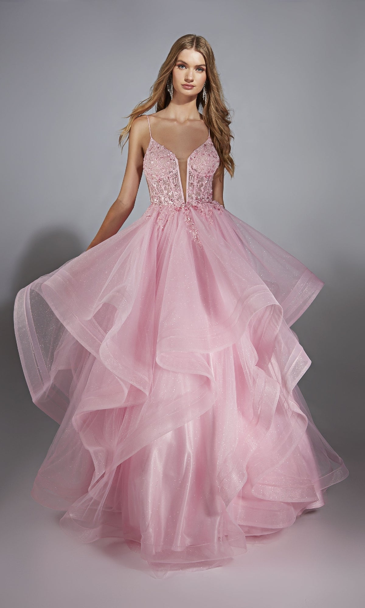 A woman wears the Alyce Paris Long Prom Dress 61731 in pink, featuring a lace embroidered corset bodice and a layered tulle skirt, standing against a plain gray background.
