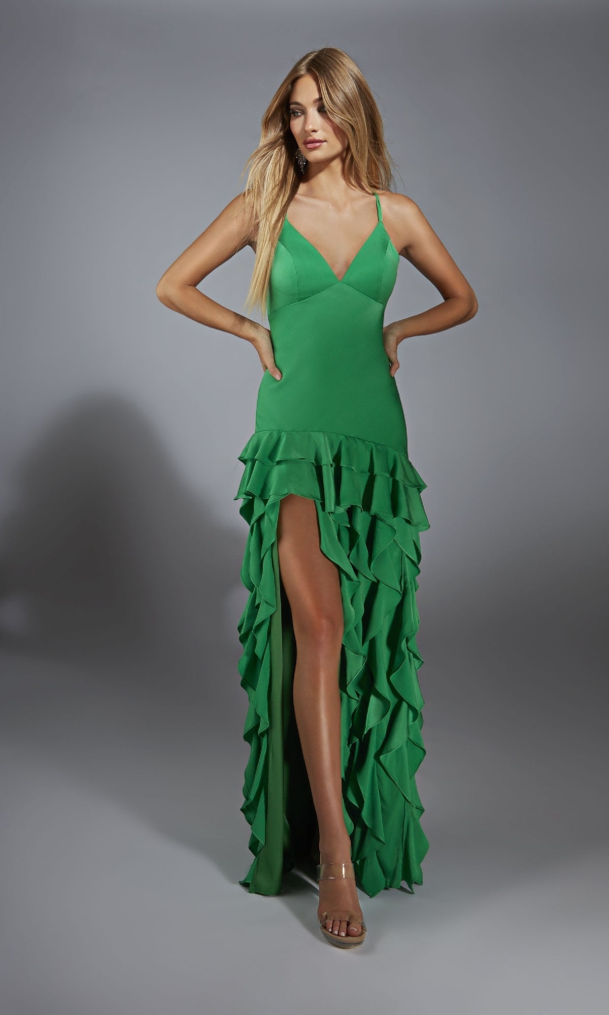 A woman models the Alyce 61737 long prom dress—a sleeveless green gown with layered ruffles and a high slit—posing against a plain gray background.