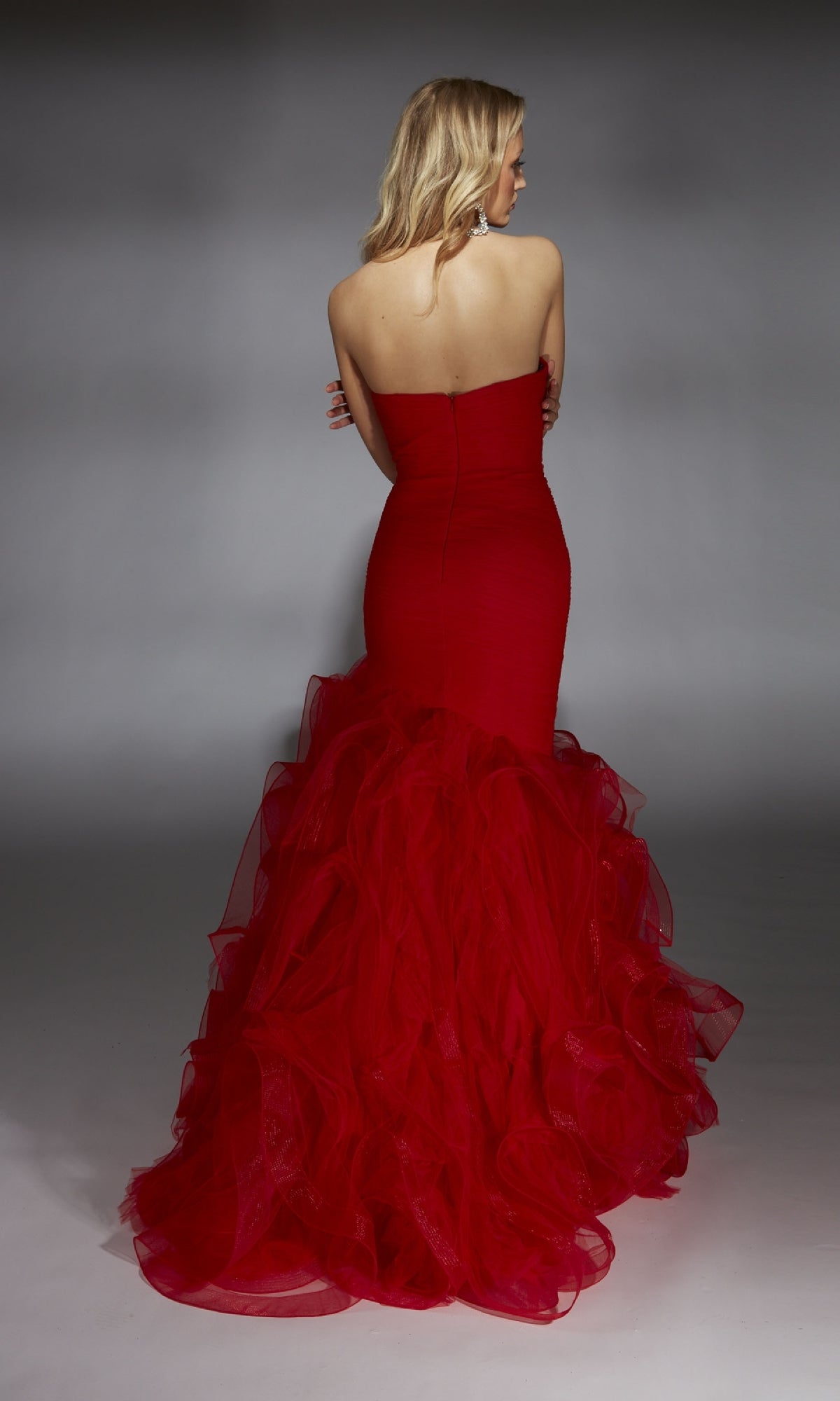 A woman in the Alyce 61739 long prom dress, featuring a strapless mermaid silhouette with a sweetheart neckline and ruffled tulle skirt, stands facing away against a plain gray background, capturing elegant style.