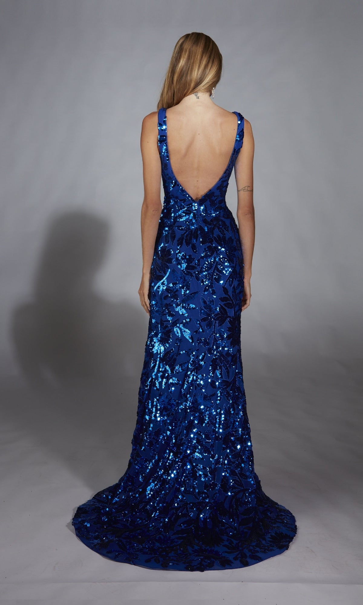A woman stands facing away against a plain gray background, wearing the Alyce 61761 Deep V-Back Long Sequin Prom Dress.