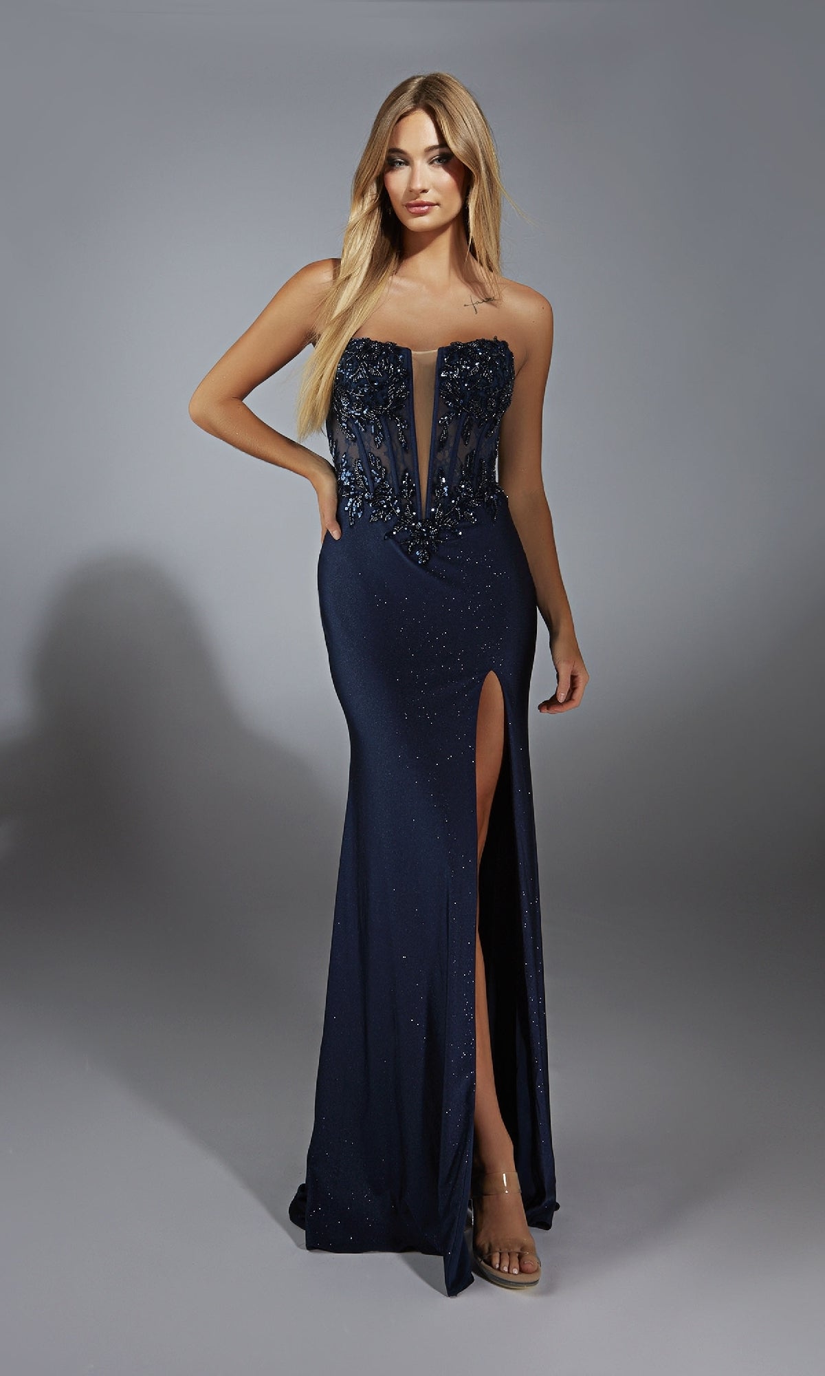 A woman wearing the Alyce 61768 long prom dress—strapless, navy blue, with a sheer illusion lace corset bodice, beaded details, and a thigh-high slit—stands against a plain gray background.