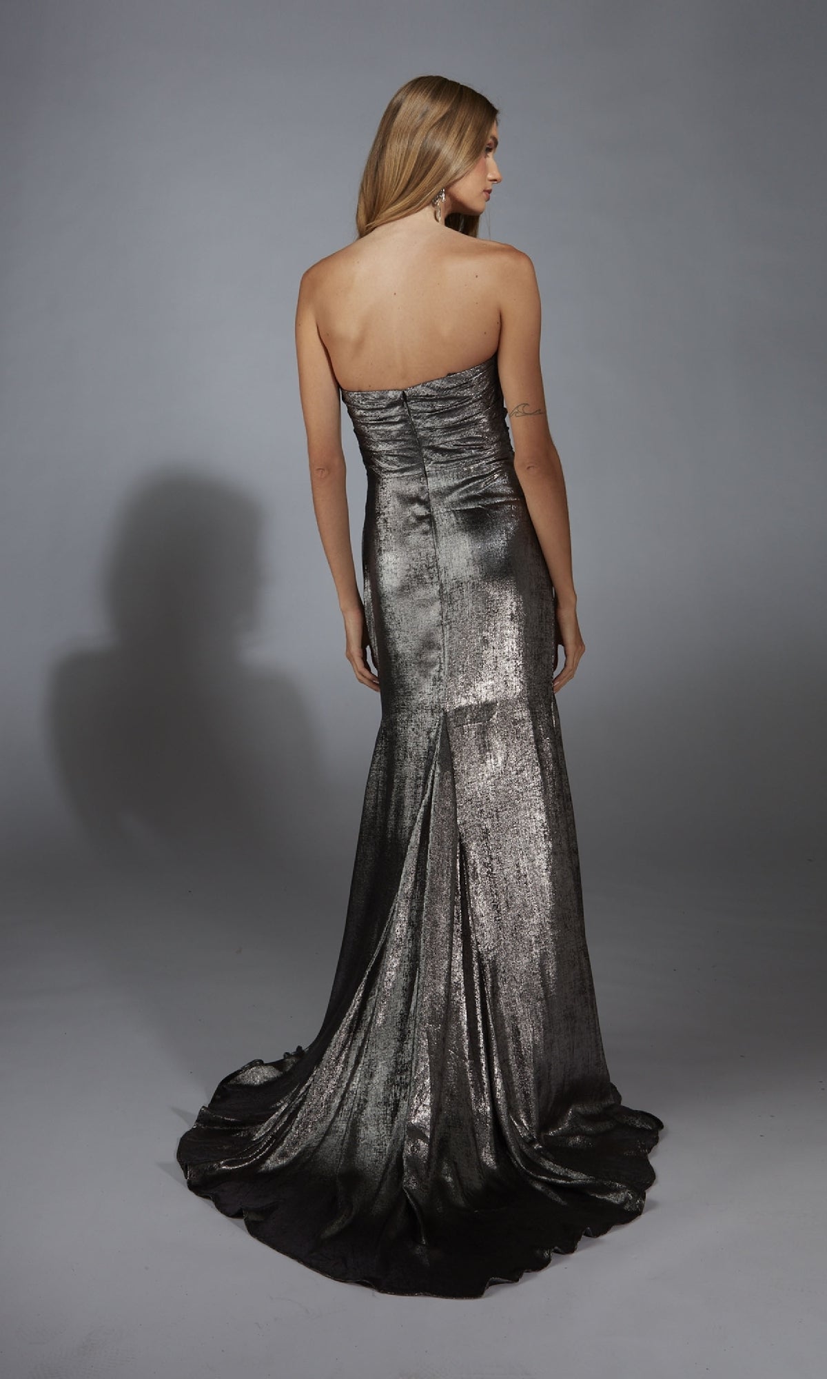 A woman in the Alyce 61778 long prom dress stands with her back to the camera, showcasing the gown’s metallic finish, fitted bodice, and elegant, flowing train.