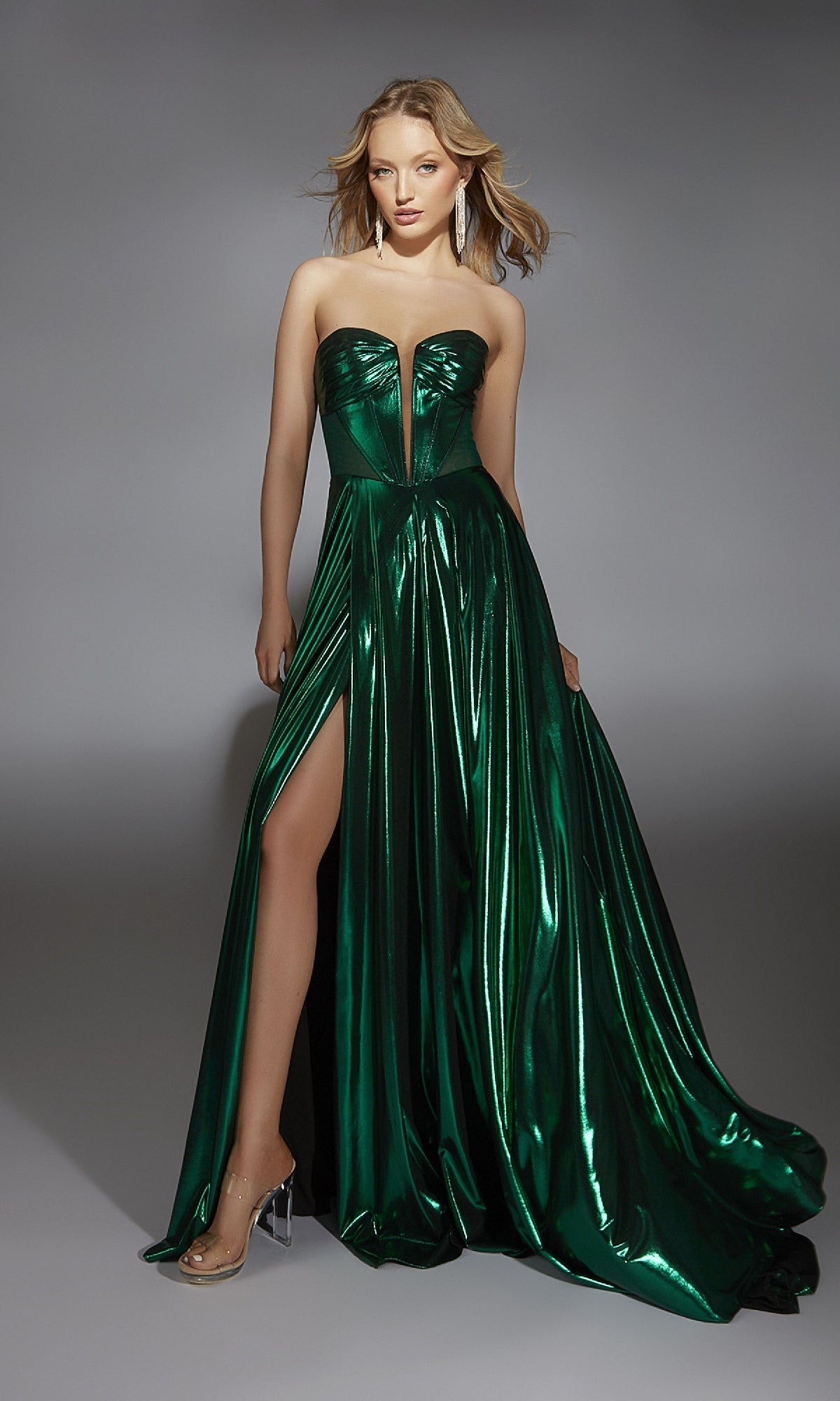 A woman poses against a gray backdrop wearing the Alyce 61797, a long strapless metallic prom dress in bold green with a front leg slit, exuding shimmering elegance.