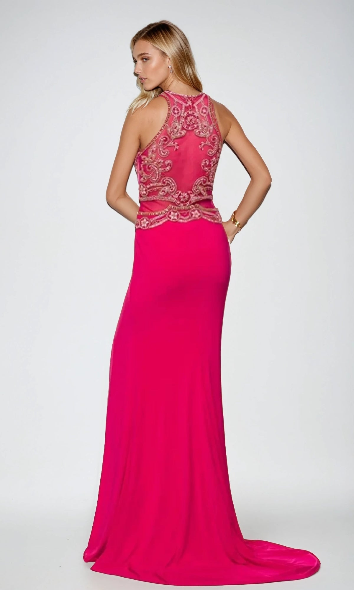 A woman wearing the Juliet 617 long prom dress, featuring a sleeveless bright pink design with a beaded bodice and embellished sheer back, stands facing away from the camera.