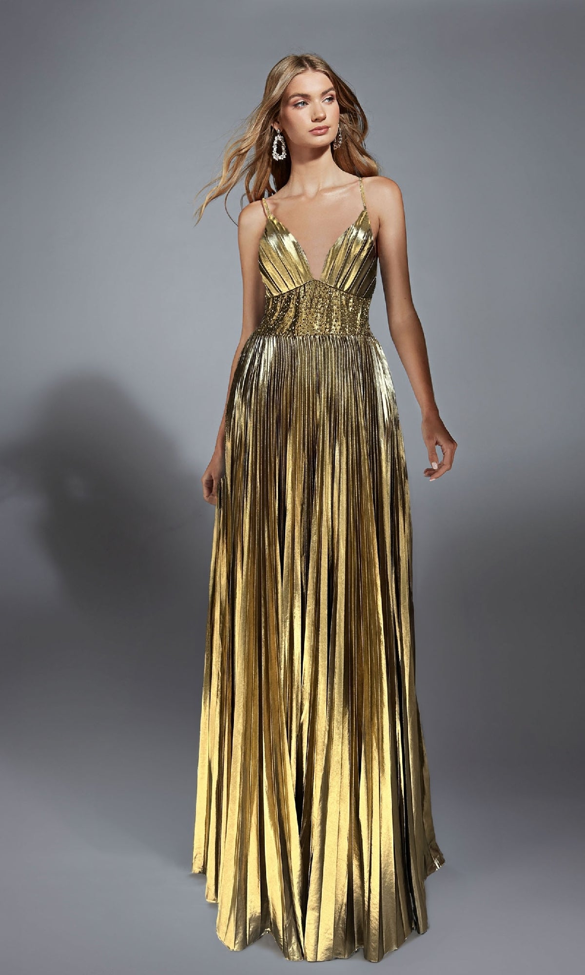 A woman wears the Alyce 61804 long prom dress with a metallic foil finish, featuring a pleated A-line skirt, thin straps, and a fitted bodice, set against a plain gray background.