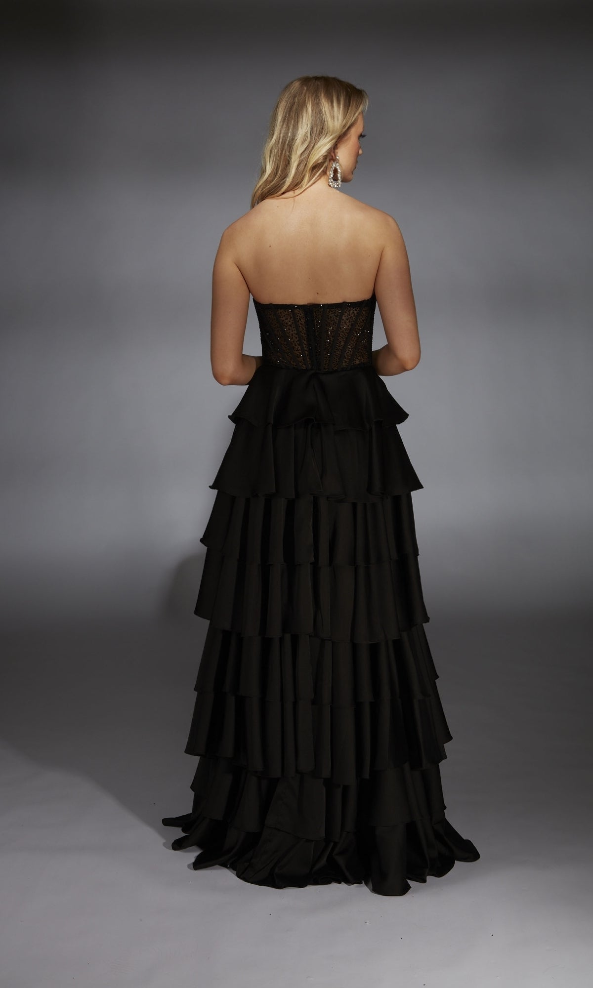A woman faces away from a neutral background wearing the Long Prom Dress: Alyce 61833, featuring a strapless fitted sheer corset bodice and a ruffle tiered A-line skirt.
