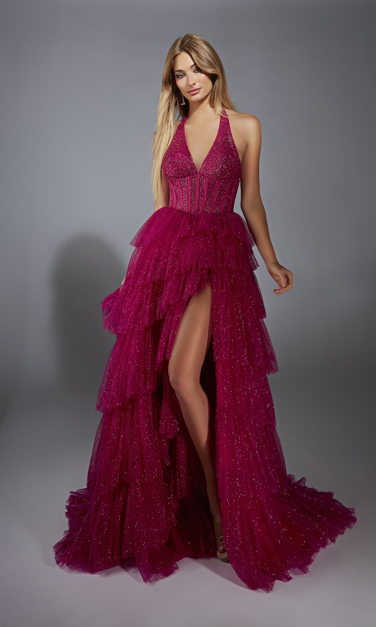 A woman poses in the Alyce 61859 Long Prom Dress—a sleeveless deep pink gown featuring a corset bodice, tiered ruffled skirt with beaded details, and a high slit—against a plain gray background.