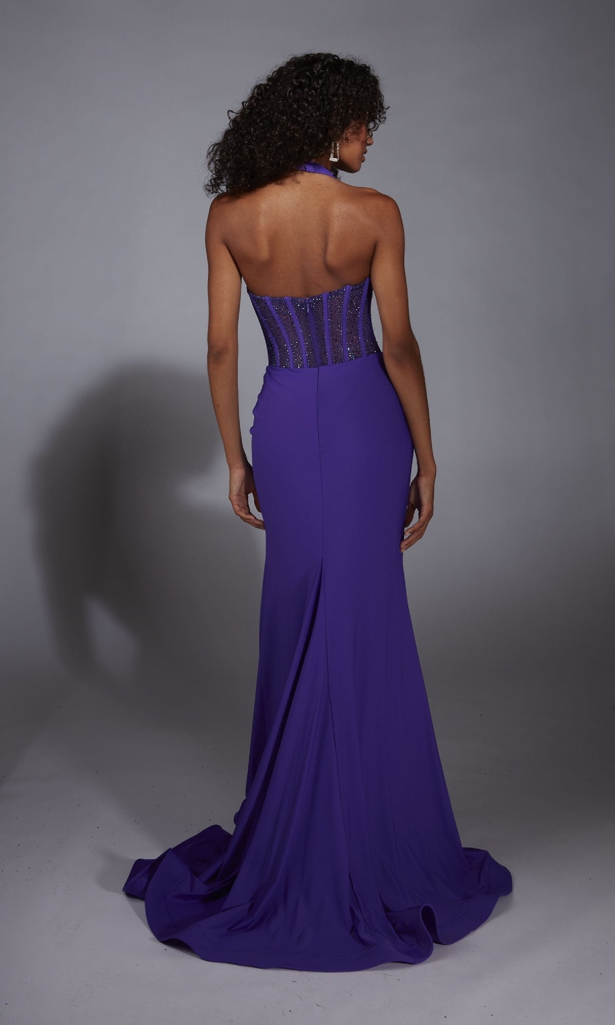 A woman models the Alyce 61860 Long Prom Dress, a floor-length strapless purple gown with a corset bodice and beaded accents, standing with her back to the camera against a plain gray background.